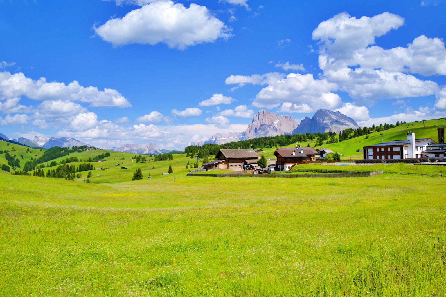 Prairie verte vibrante sous un ciel bleu avec des nuages moelleux présentant des fermes et des montagnes
