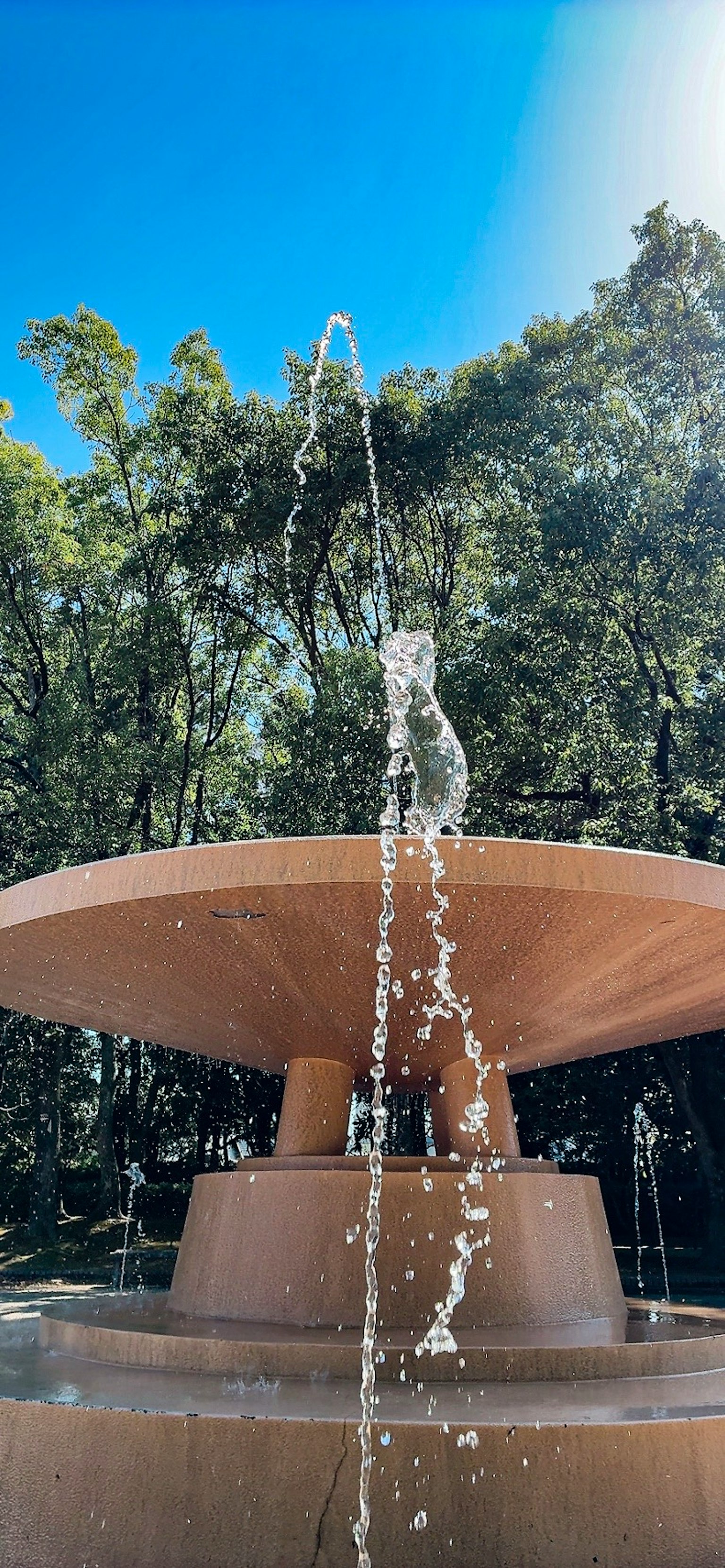青空の下で水が噴き出す噴水の近景 緑の木々が背景にある