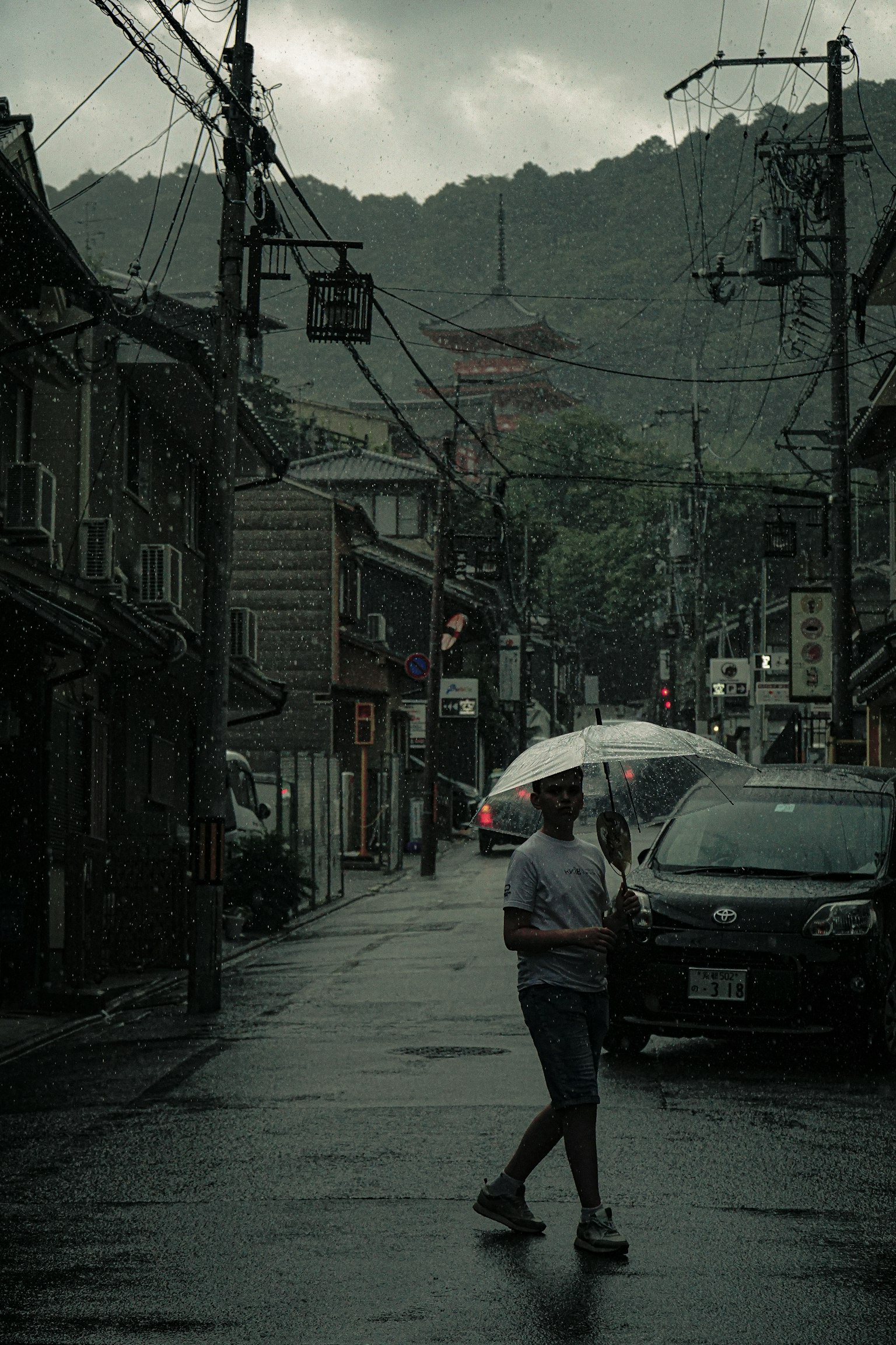 一个人在雨中走，手里拿着伞，街道两旁是老旧建筑