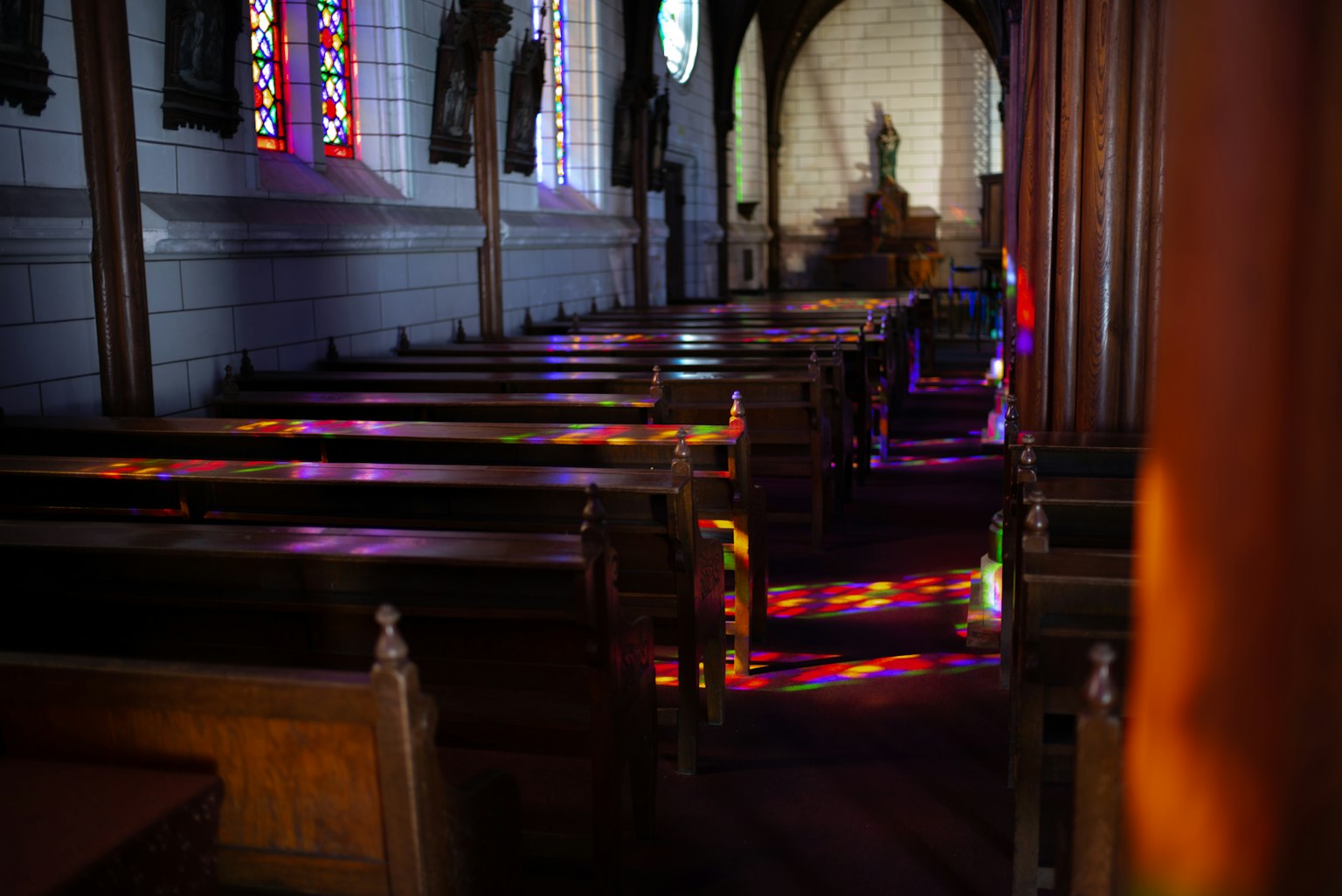 Interno di una chiesa con panche lunghe e luce colorata proveniente dalle vetrate