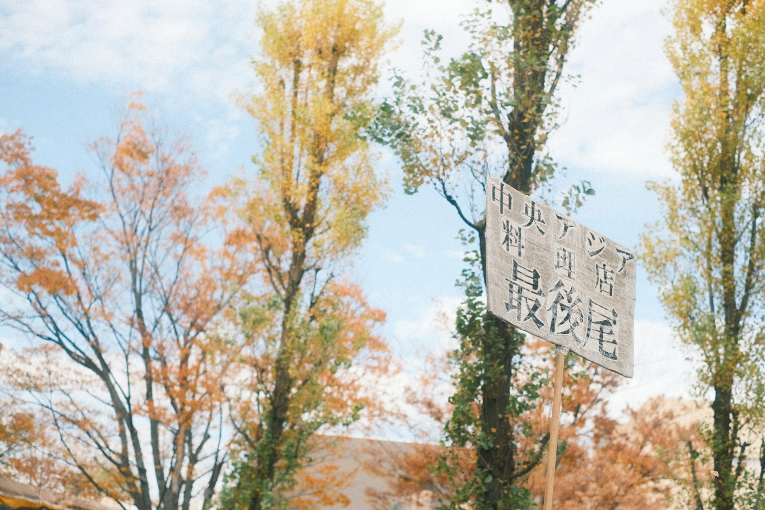 Scena autunnale con alberi gialli e cielo blu con un cartello in kanji
