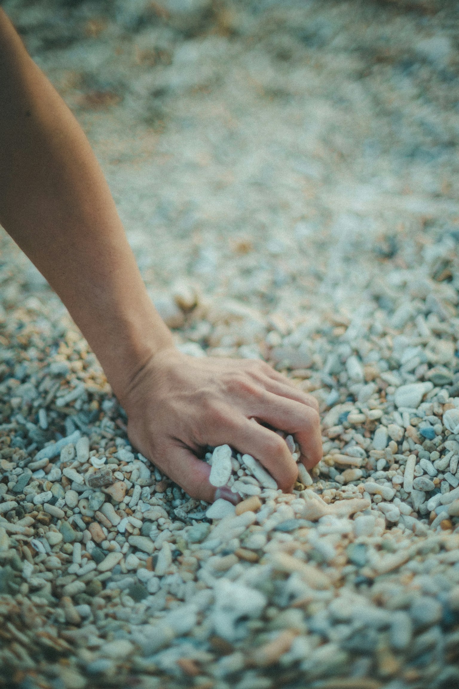 A hand reaching into a bed of pebbles