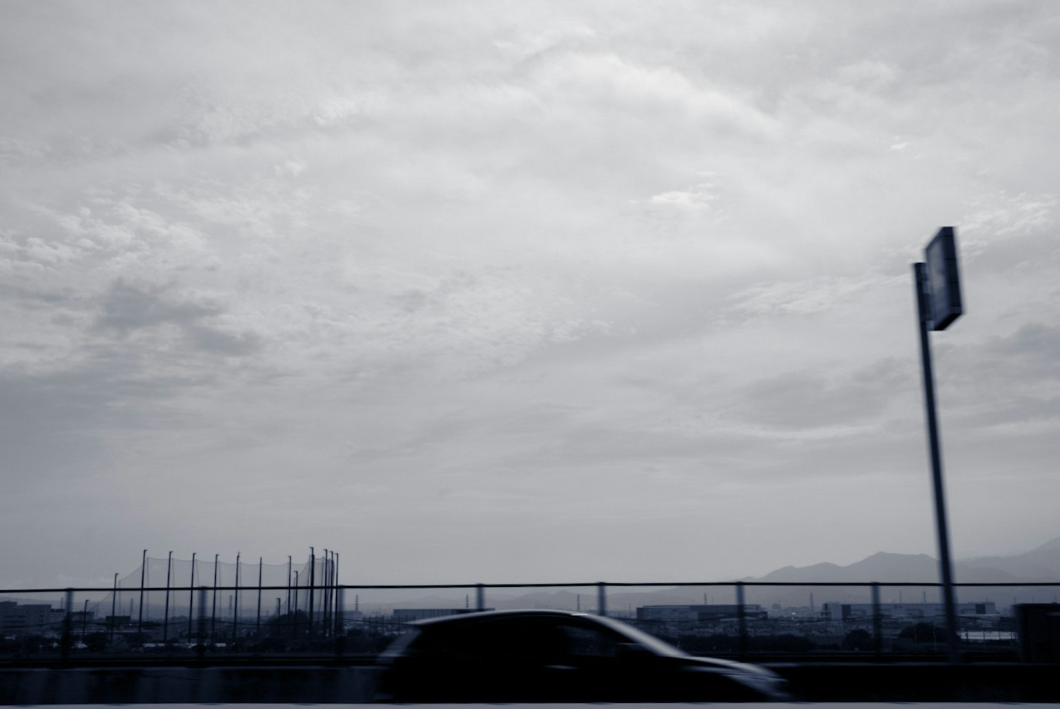 單色城市風景 汽車經過 高速公路標誌在前景 天空和建築被陰暗的雲層覆蓋