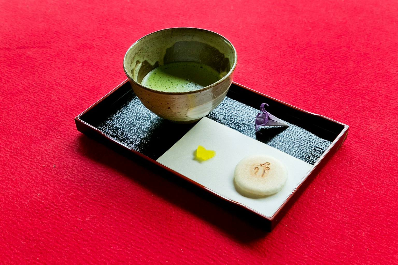 Piring hitam dengan teh matcha dan kue tradisional Jepang di latar belakang merah