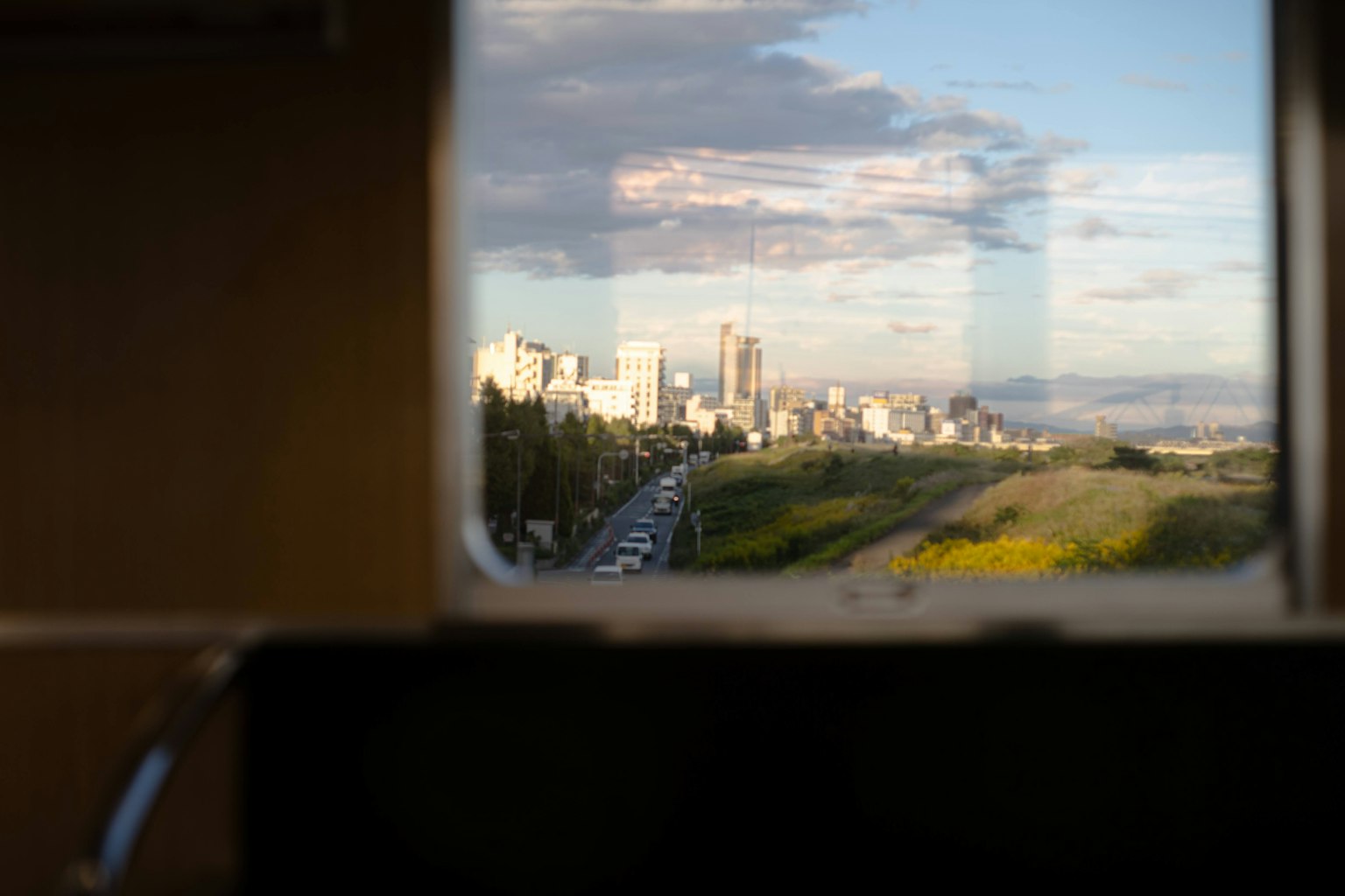 Paisaje urbano visto a través de una ventana, cielo azul con nubes, vegetación y tráfico