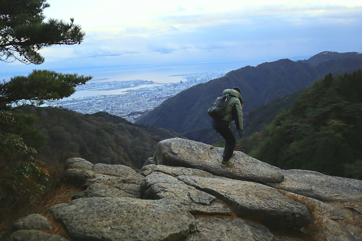 Hiker walking on rocky mountain top with blue sky and clouds overlooking distant city