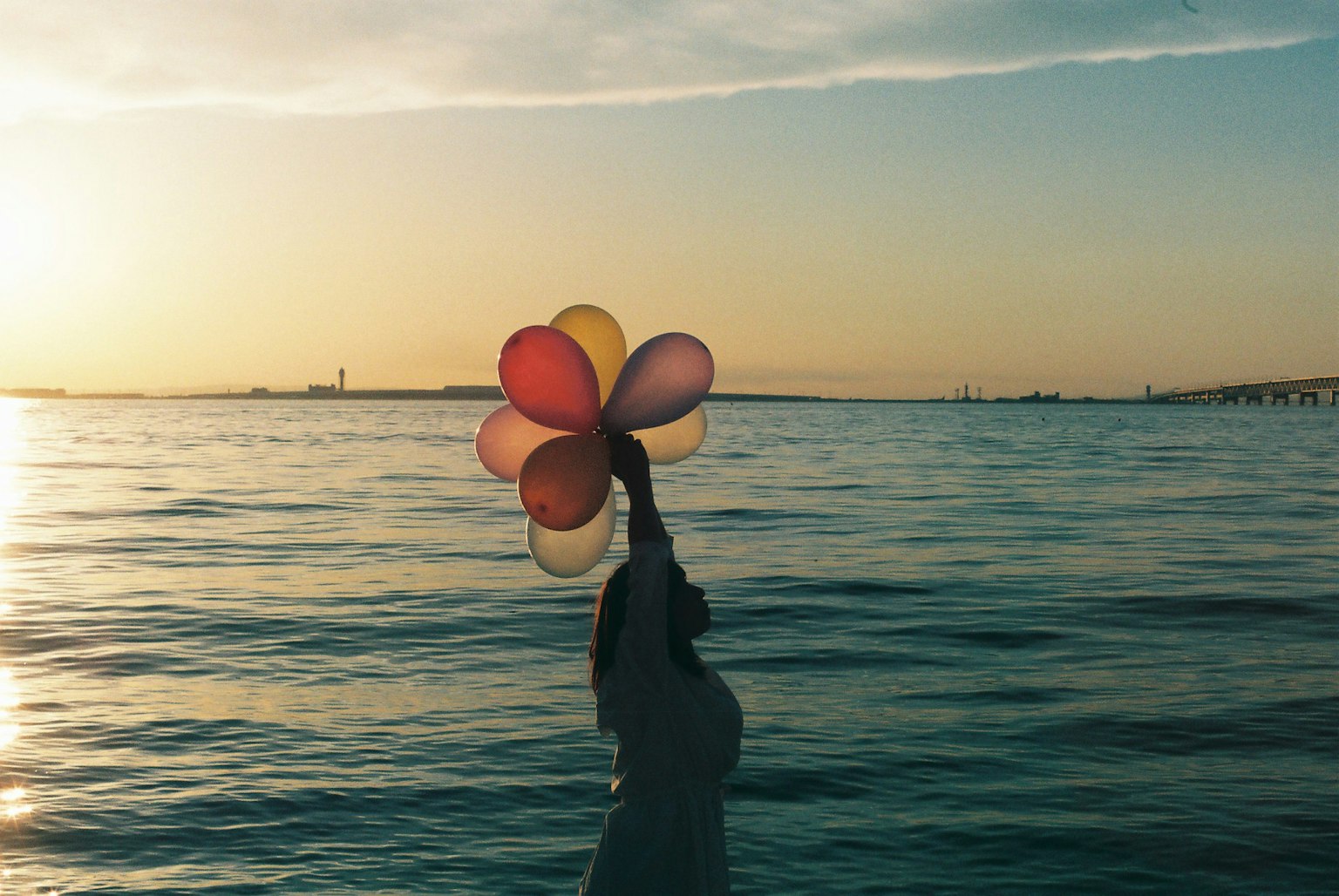 Mujer sosteniendo globos de colores contra un atardecer sobre el mar