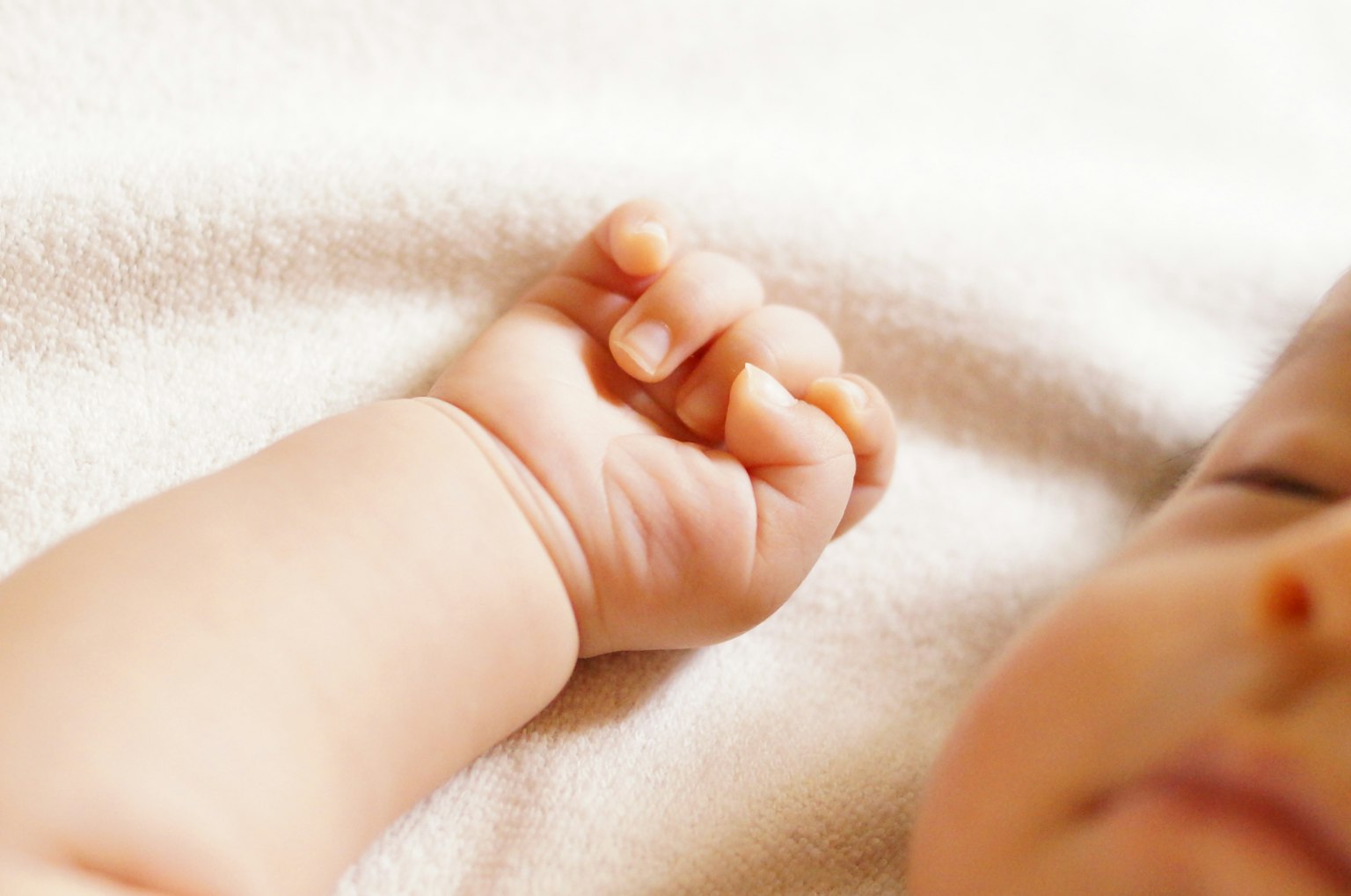 Tangan kecil bayi beristirahat di atas kain putih