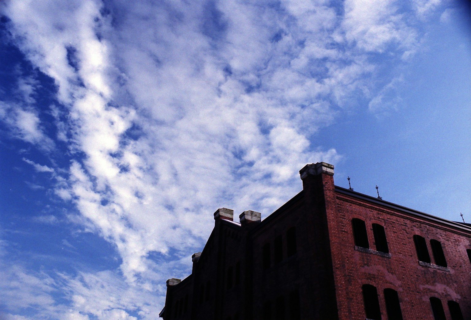Silueta de un edificio rojo contra un cielo azul con nubes blancas