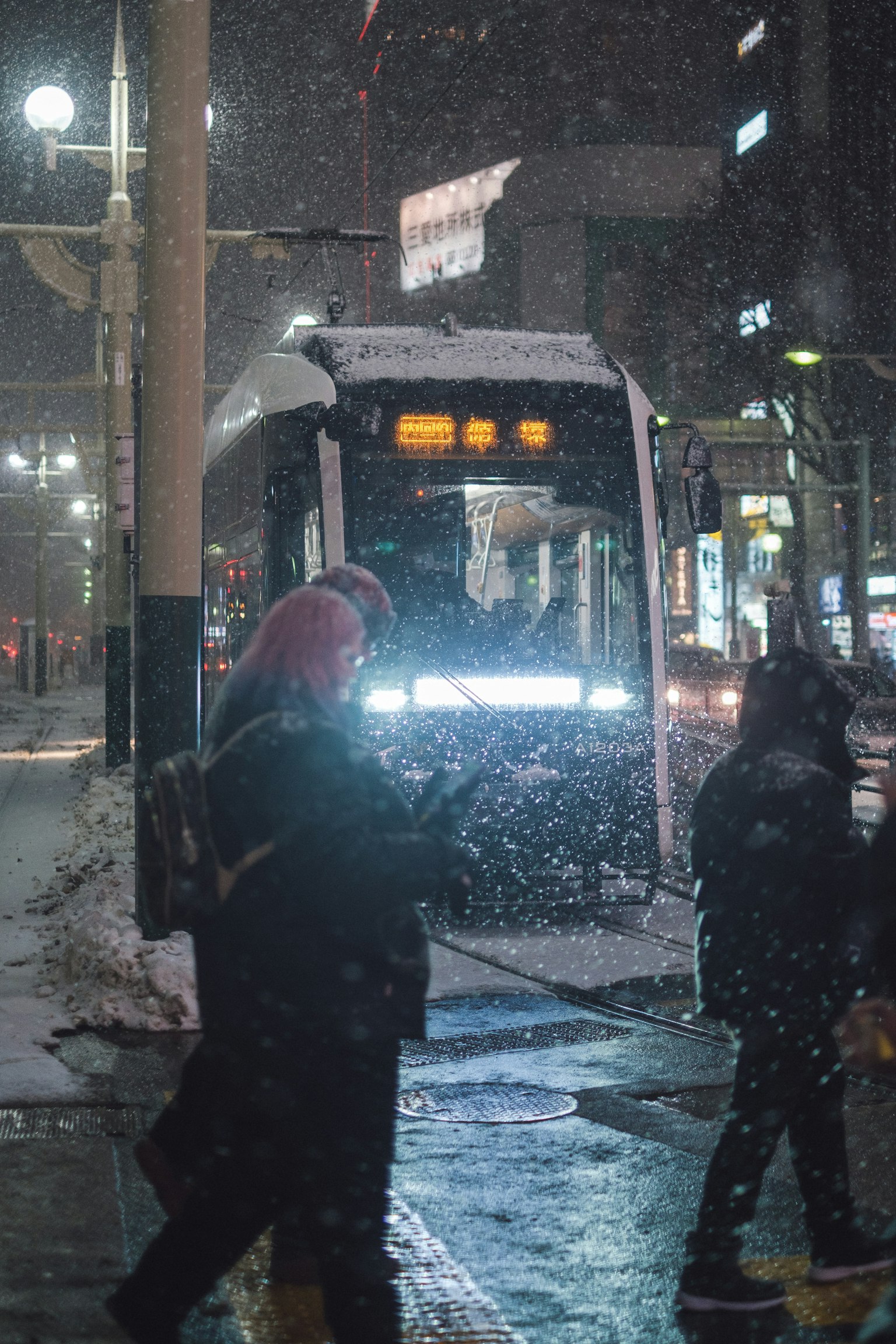 Des personnes attendant un bus dans une ville enneigée la nuit avec un bus recouvert de neige