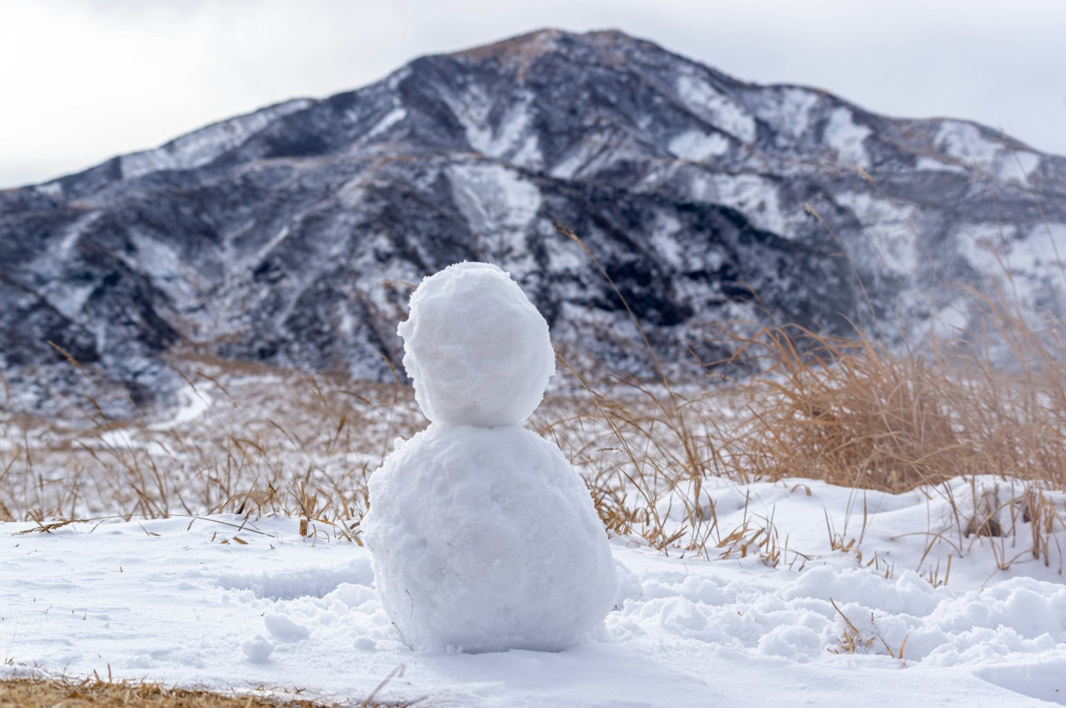 一个雪人在雪上坐着，背景是山