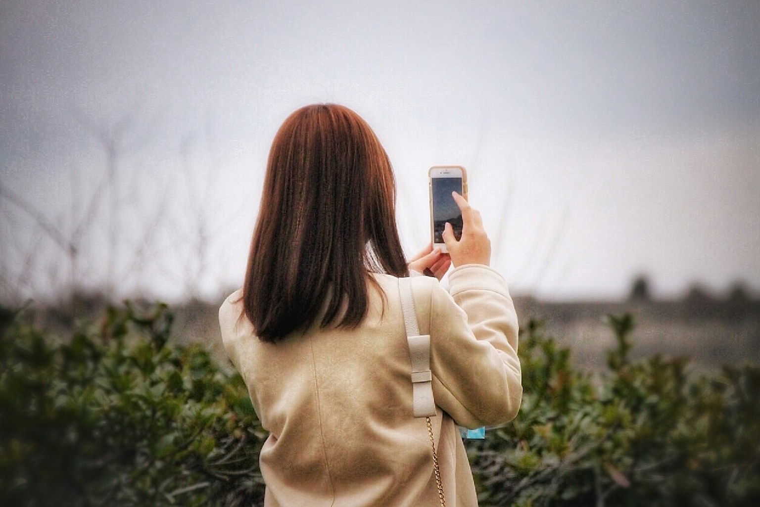 Wanita mengambil foto dengan smartphone di bawah langit mendung