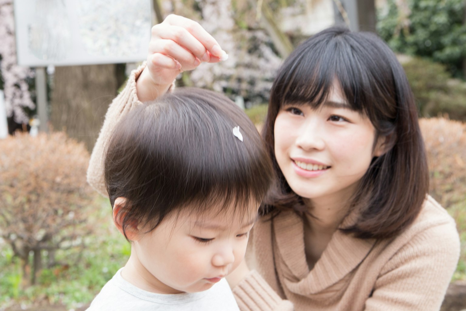 Une mère mettant un pétale de fleur sur les cheveux de son enfant dans un parc