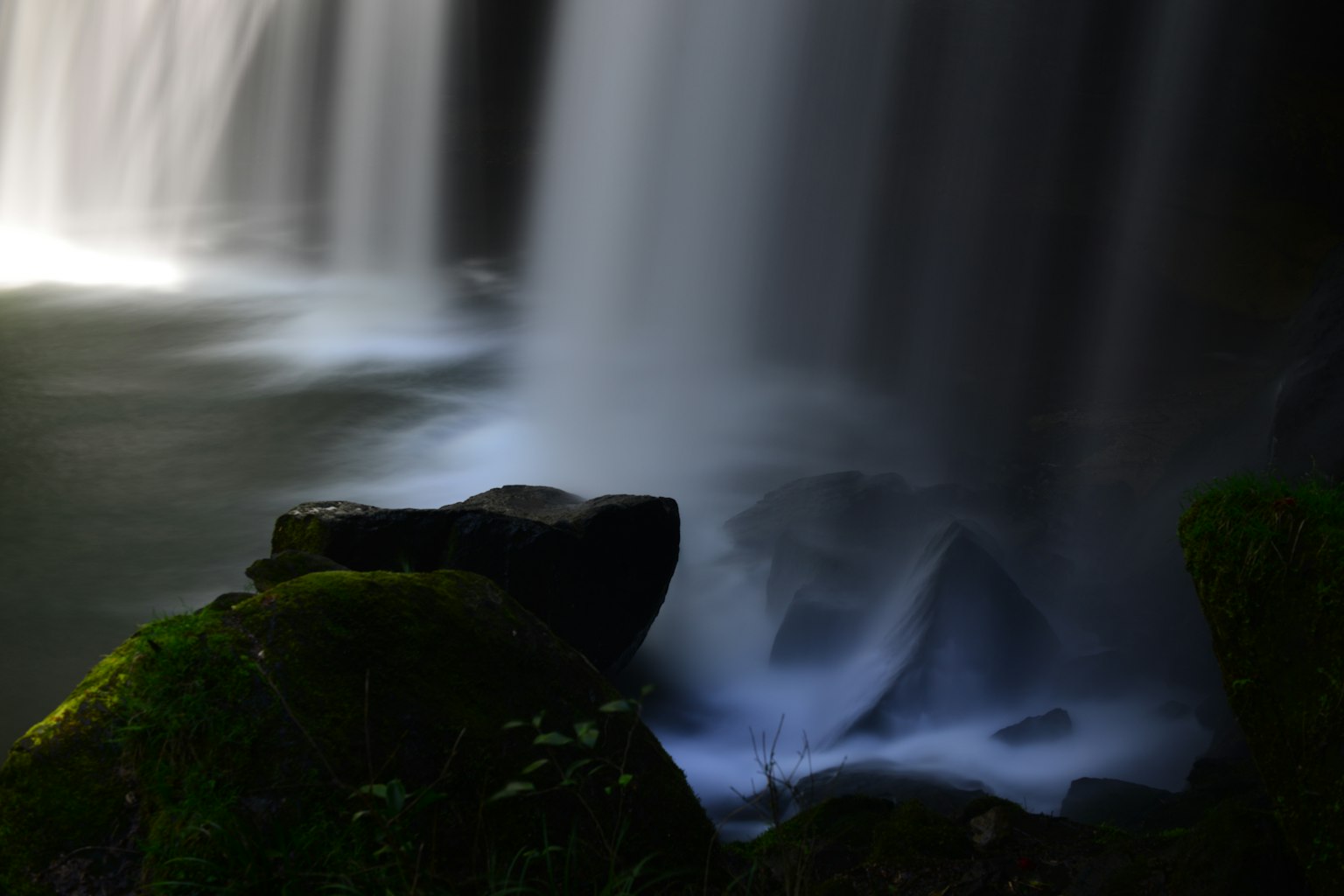 Primer plano de una roca junto a una cascada con agua fluyendo