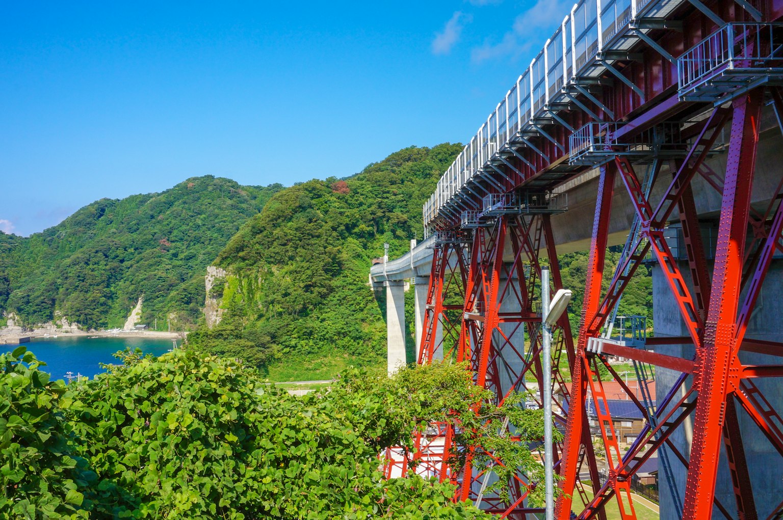 Pont en acier rouge avec des montagnes verdoyantes sous un ciel bleu
