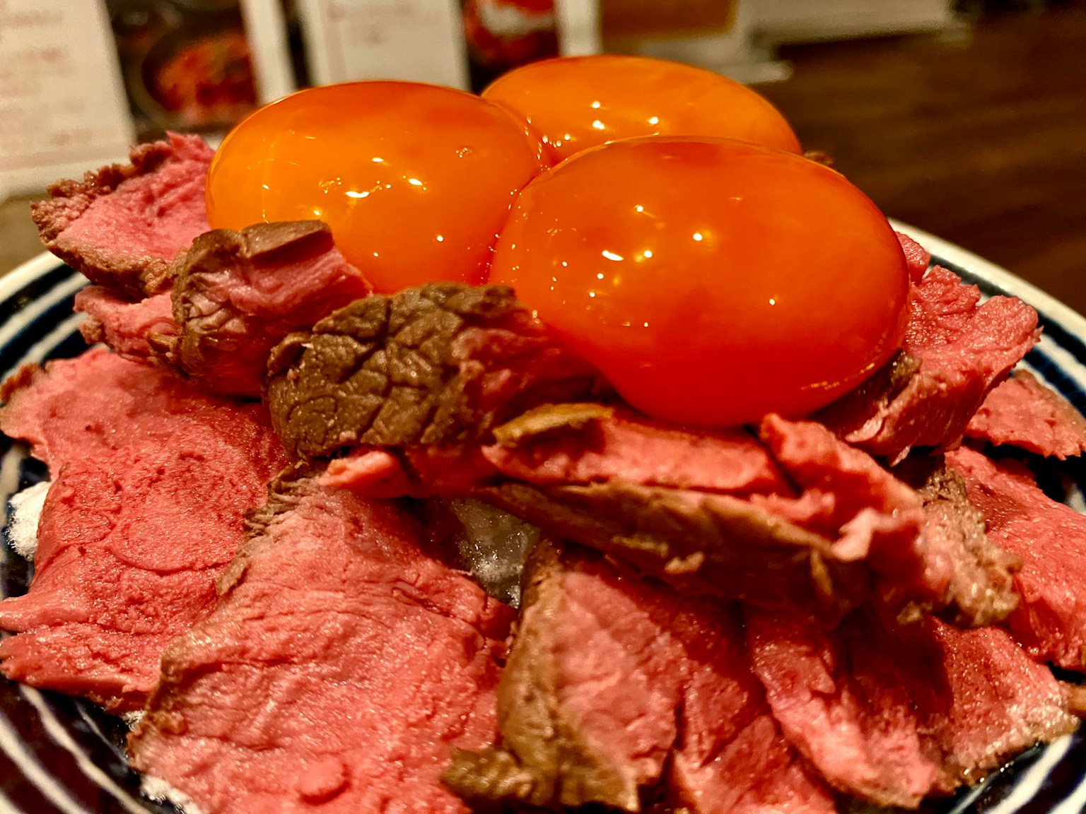 一盘切片烤牛肉，上面放着三个蛋黄