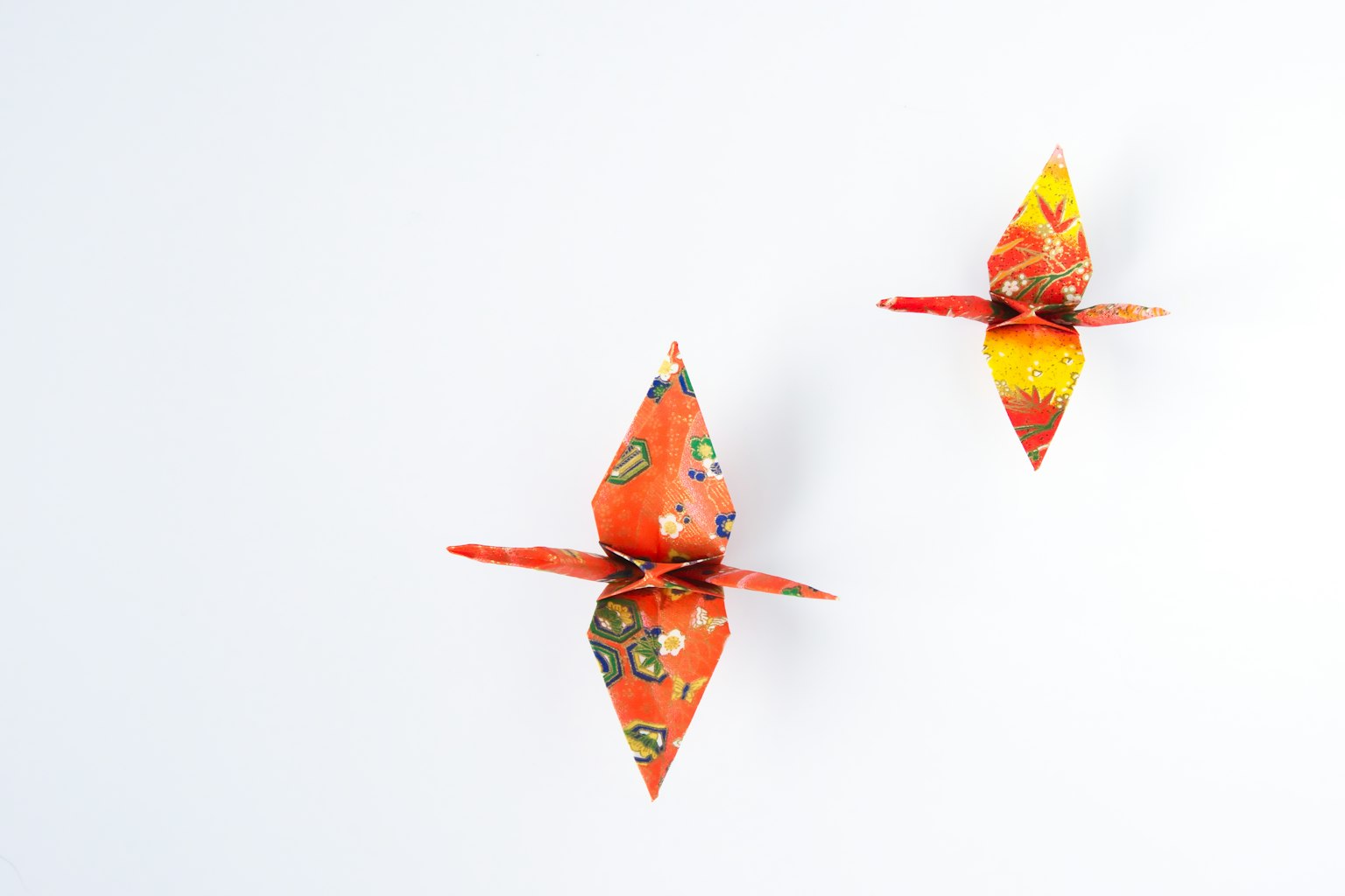 Zwei lebendige orangefarbene Origami-Kraniche auf einem weißen Hintergrund