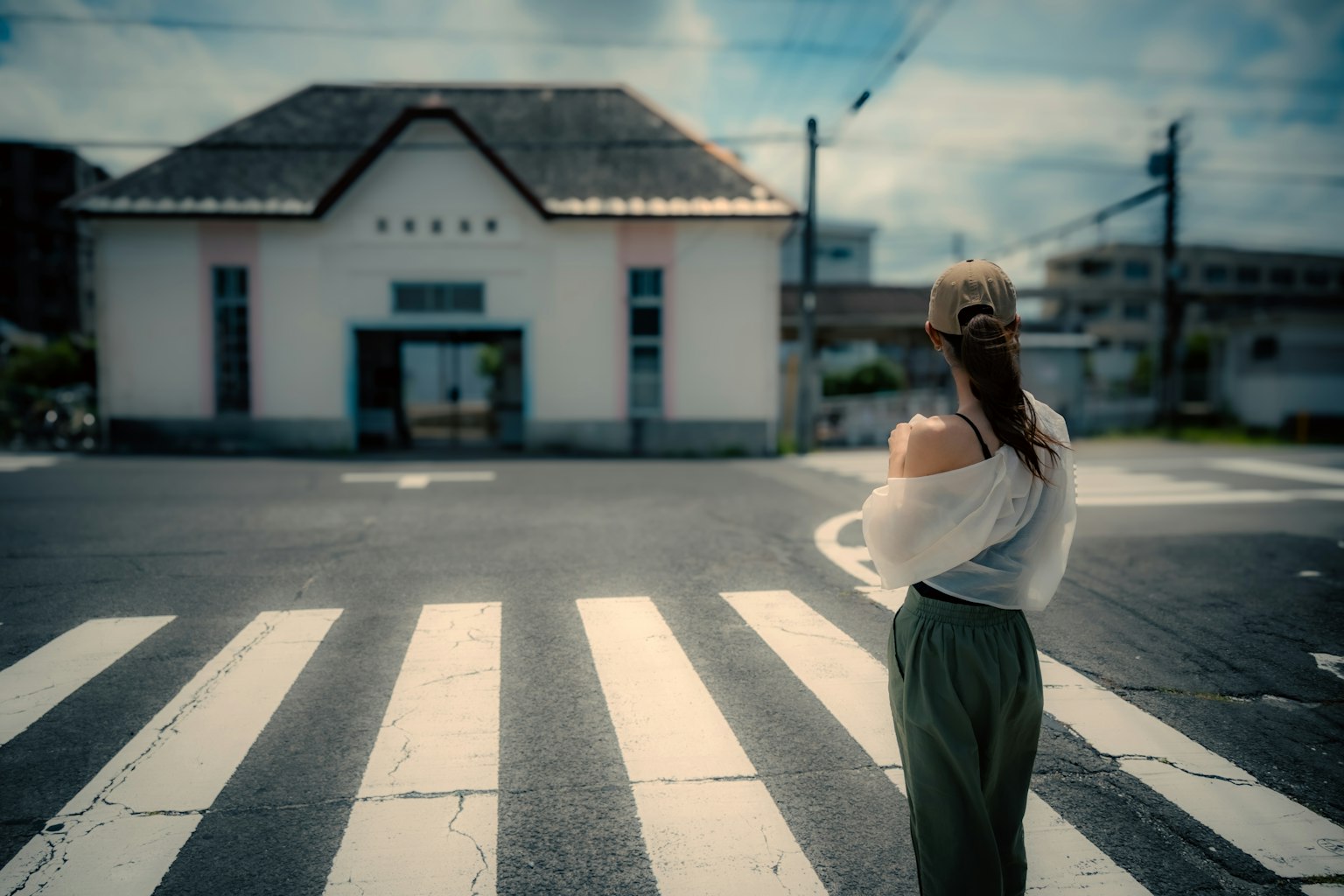 A woman standing with her back to the camera in front of a white building at a crosswalk elegant posture under a blue sky
