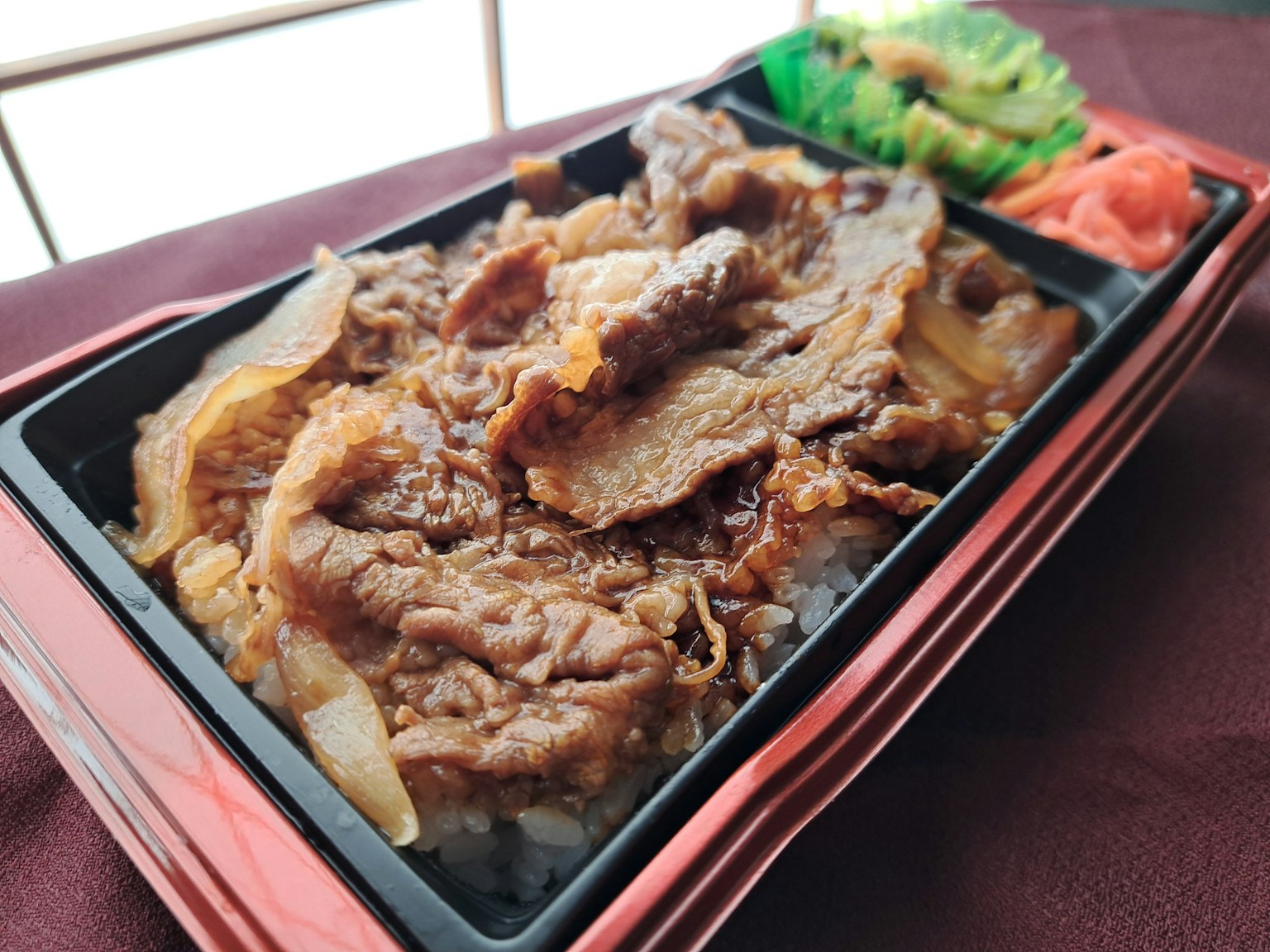 お弁当の中に牛肉と玉ねぎが乗ったご飯があり、サイドに野菜が添えられている