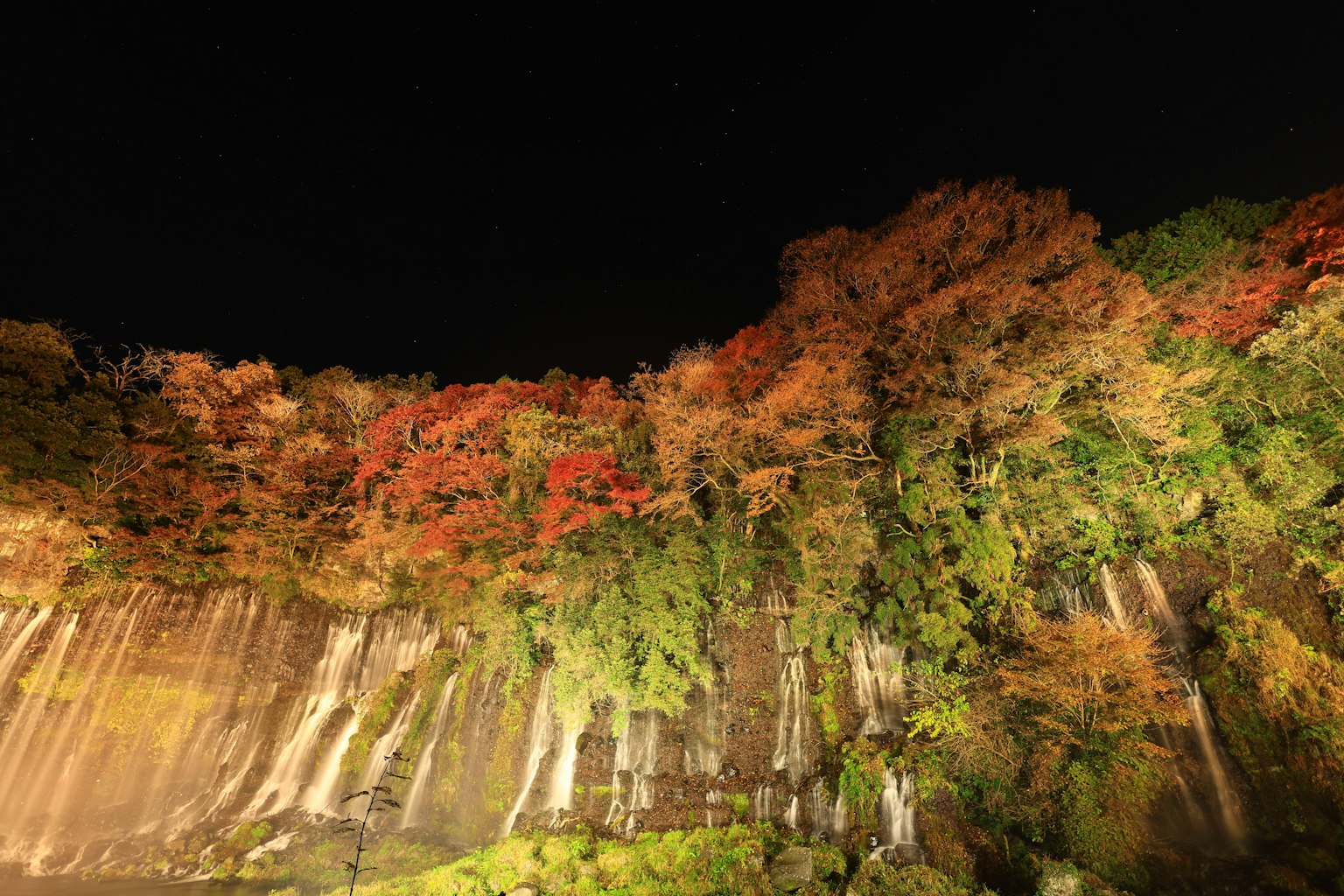 Nachtansicht eines Wasserfalls mit lebhaftem Herbstlaub