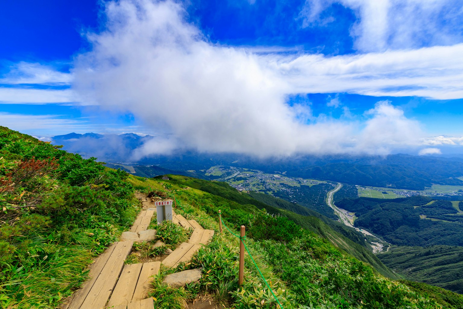 Paesaggio montano con cielo blu e nuvole prato verde e sentiero in legno