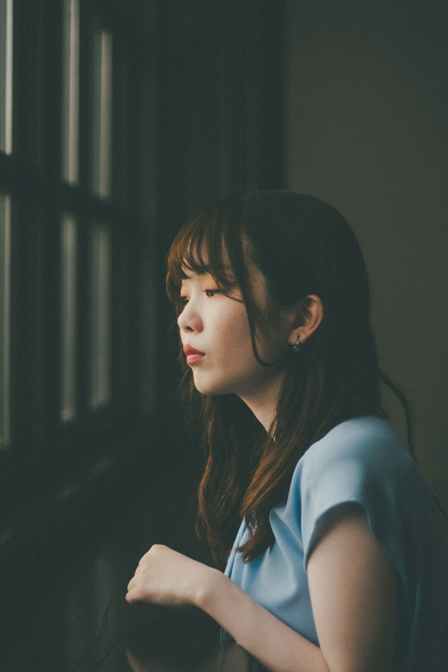 Hình ảnh nghiêng của người phụ nữ trong áo xanh nhìn ra ngoài cửa sổ