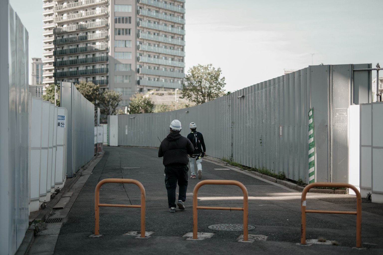 Two workers walking down a construction site pathway with a high-rise building in the background