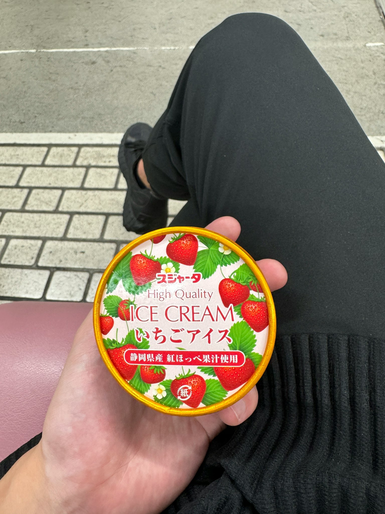 手握着草莓冰淇淋杯穿着黑裤子