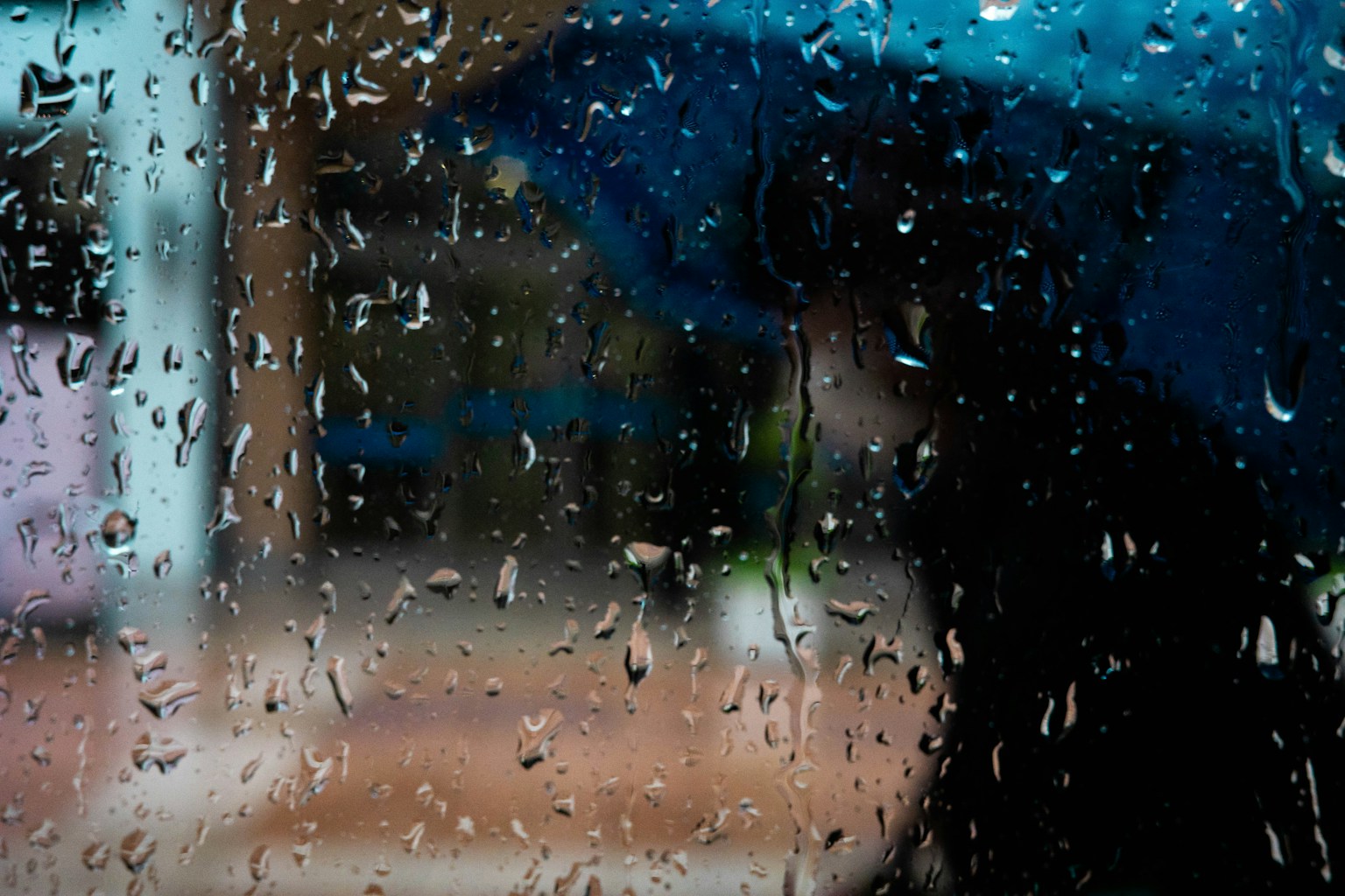 透過雨水浸濕的窗戶看到的藍傘人影