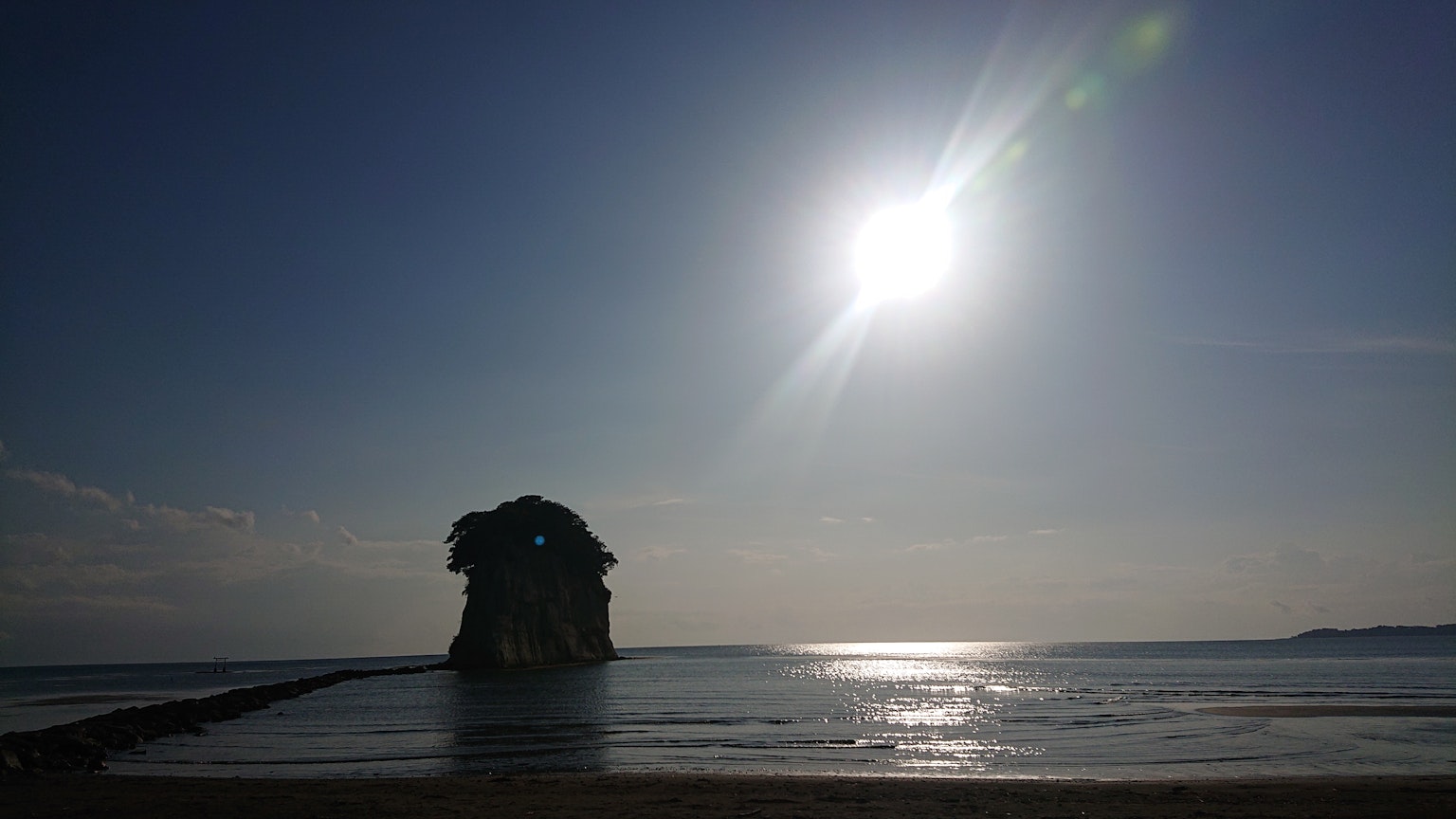 Ein großer Felsen im Ozean mit Sonnenlicht, das sich auf ruhigem Wasser spiegelt