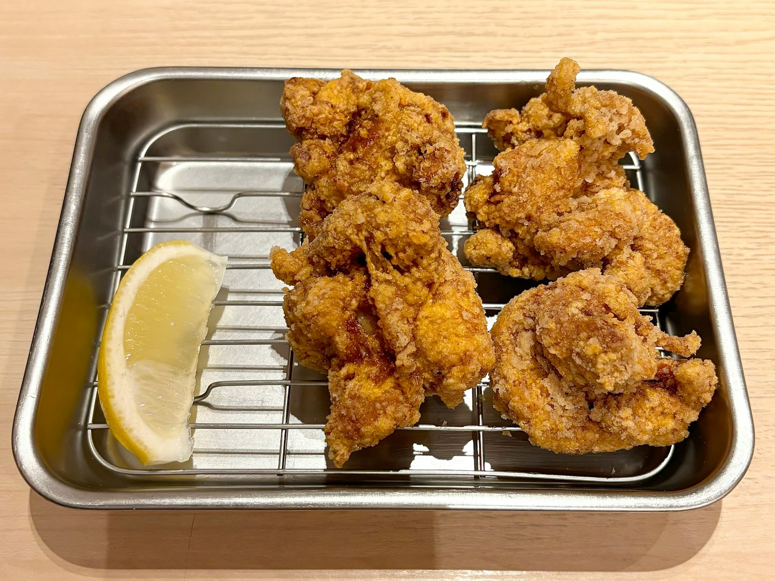 Crispy fried chicken served on a metal tray with a slice of lemon