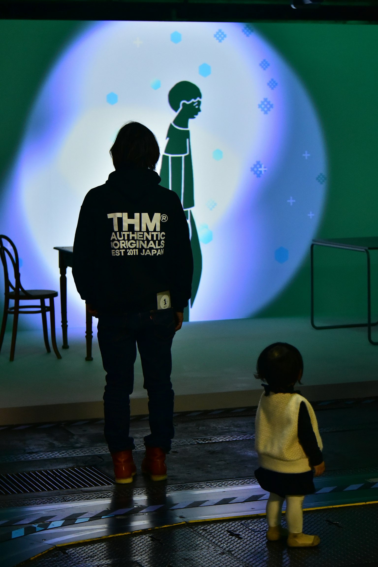 背を向けた大人と子供がアニメーションの背景を見つめているシーン