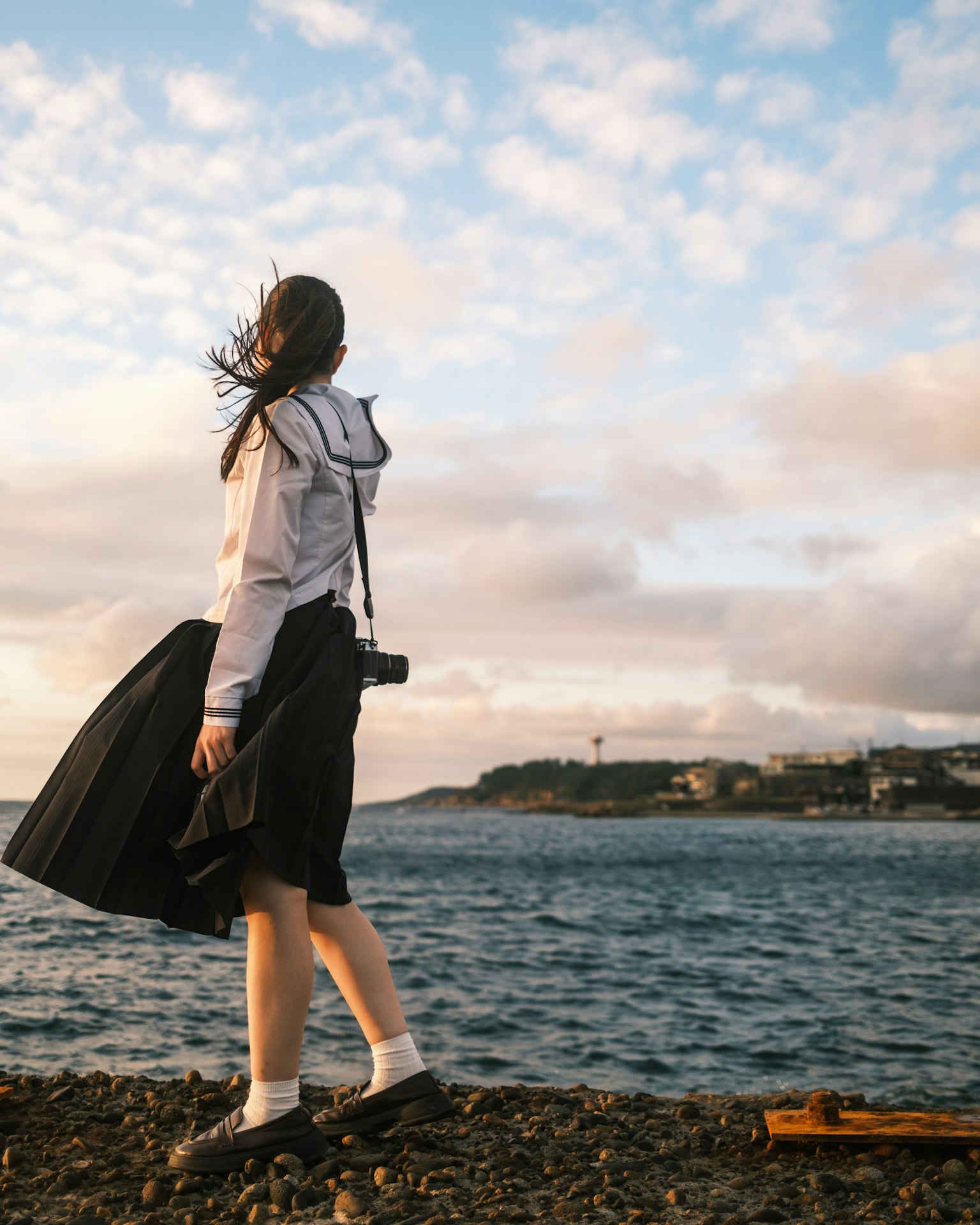 海辺で風に吹かれる女性の後ろ姿 青空と雲が広がる風景