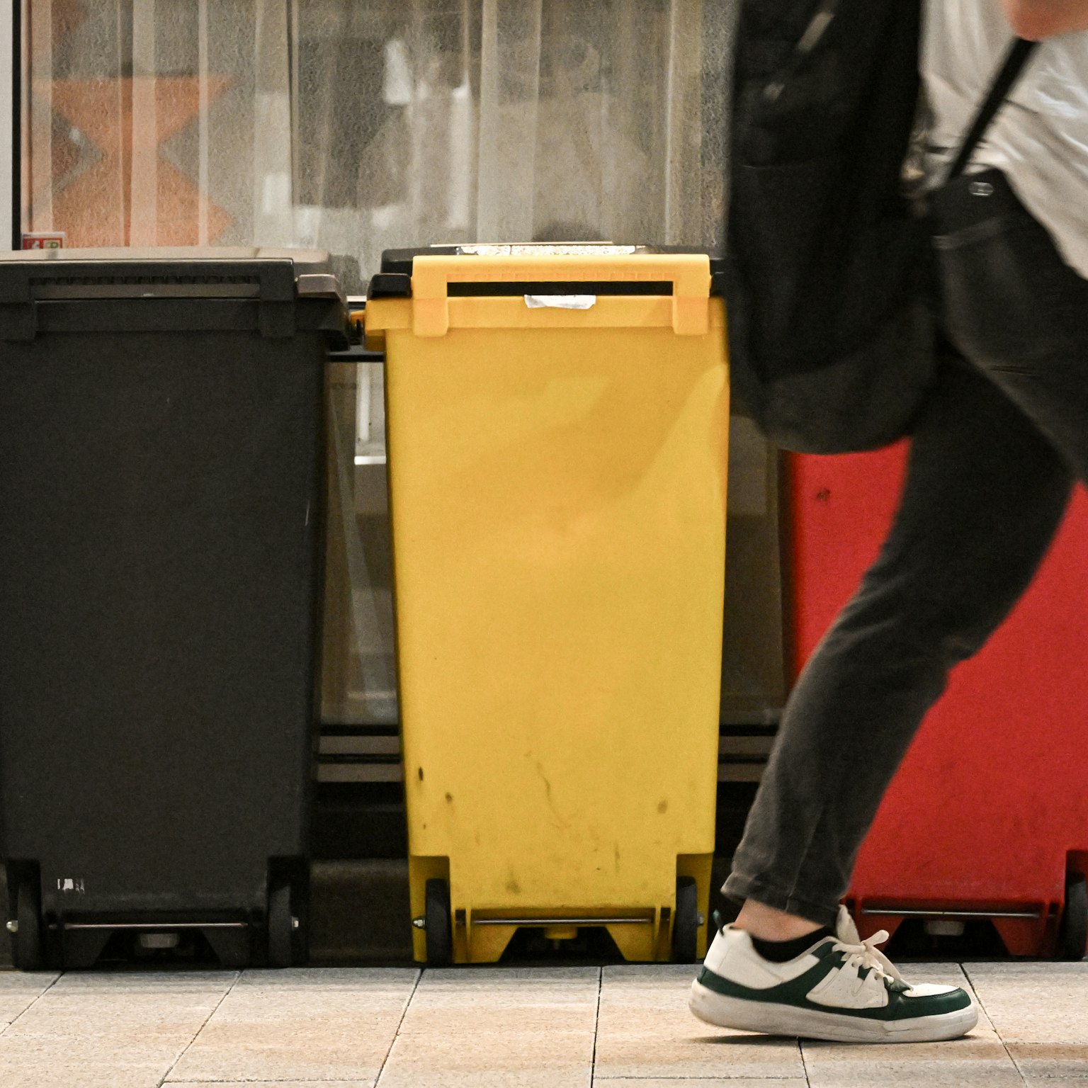 Barisan tempat sampah hitam, merah, dan kuning dengan seseorang yang berjalan