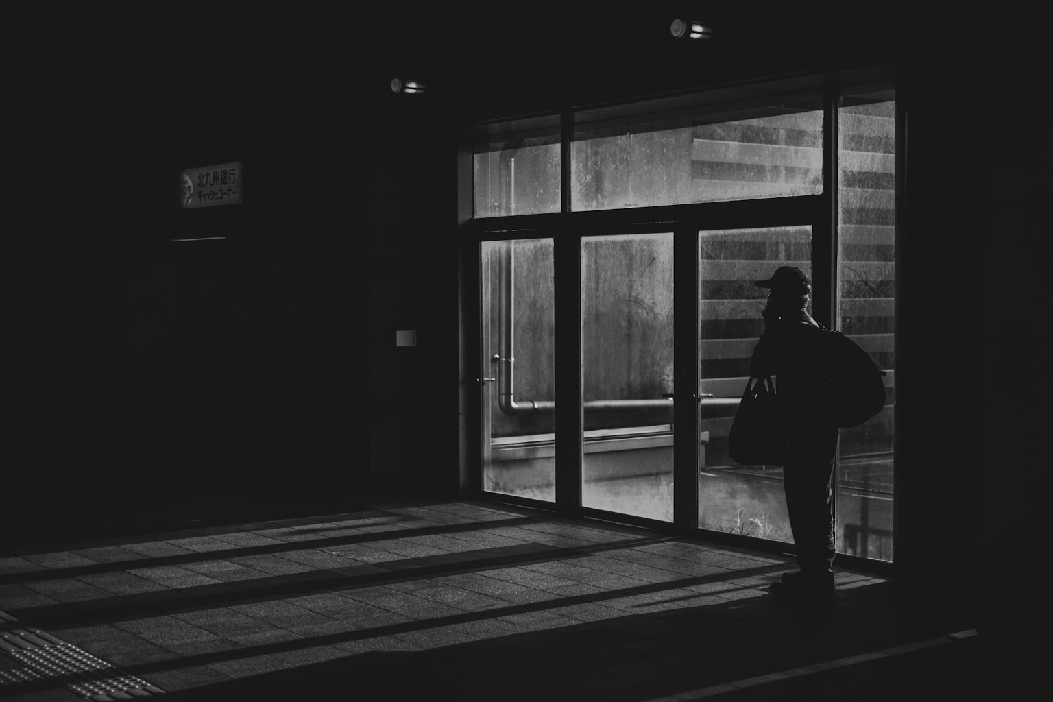 Silhouette di una persona davanti a una porta in vetro illuminata di notte