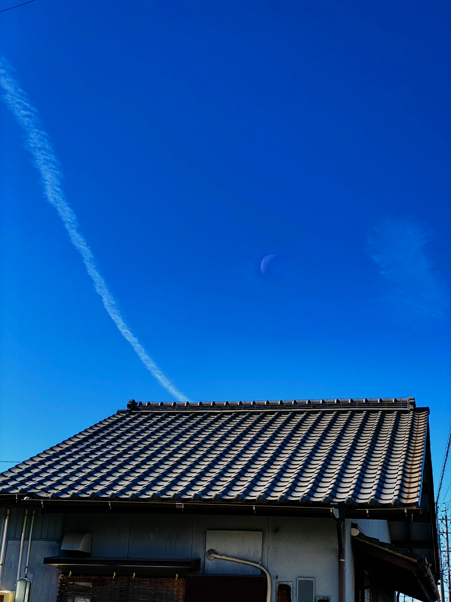 在晴朗蓝天下的传统日本房屋屋顶和白色飞机尾迹