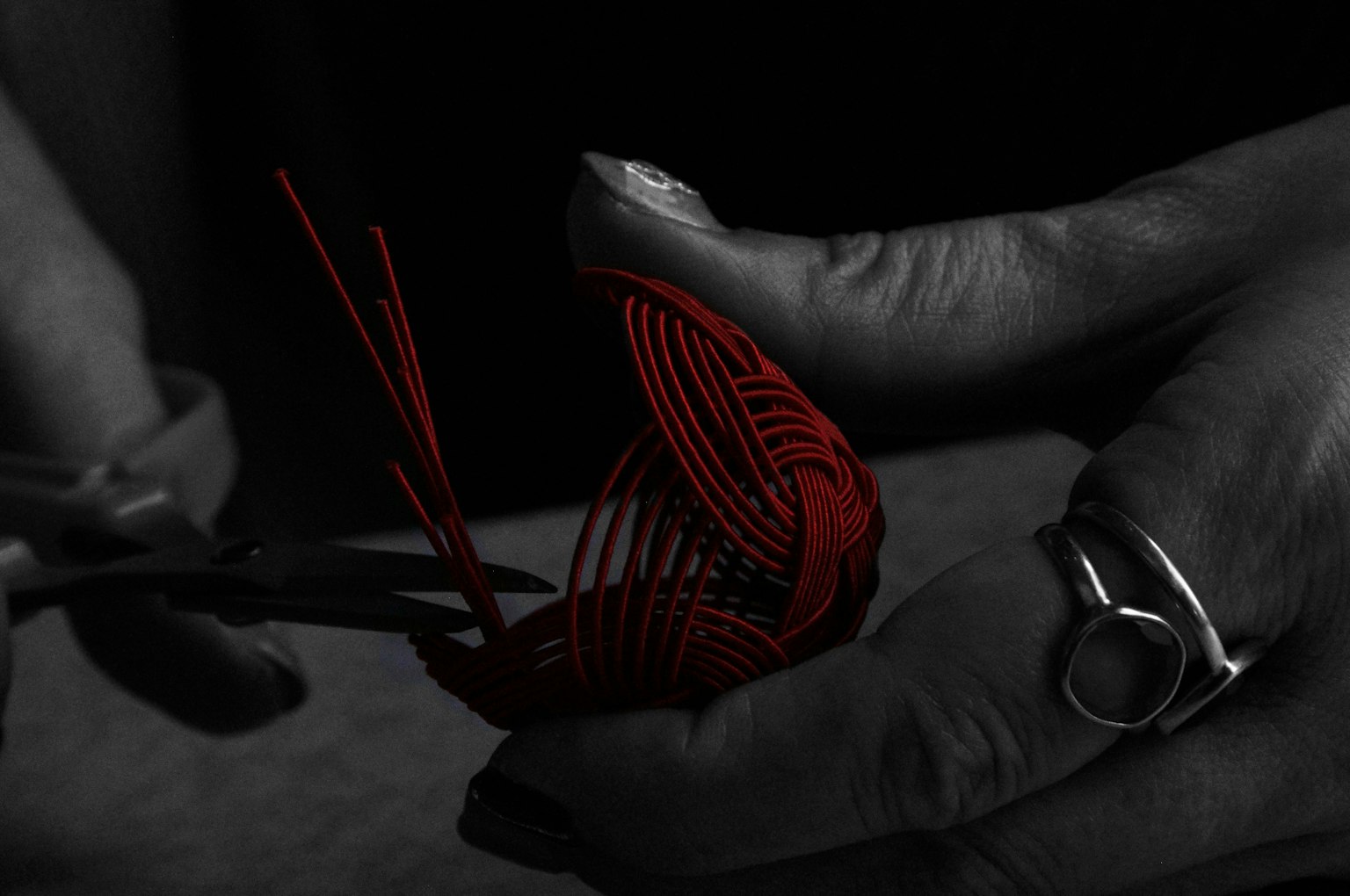 Primer plano de manos cortando hilo rojo con tijeras sobre fondo oscuro