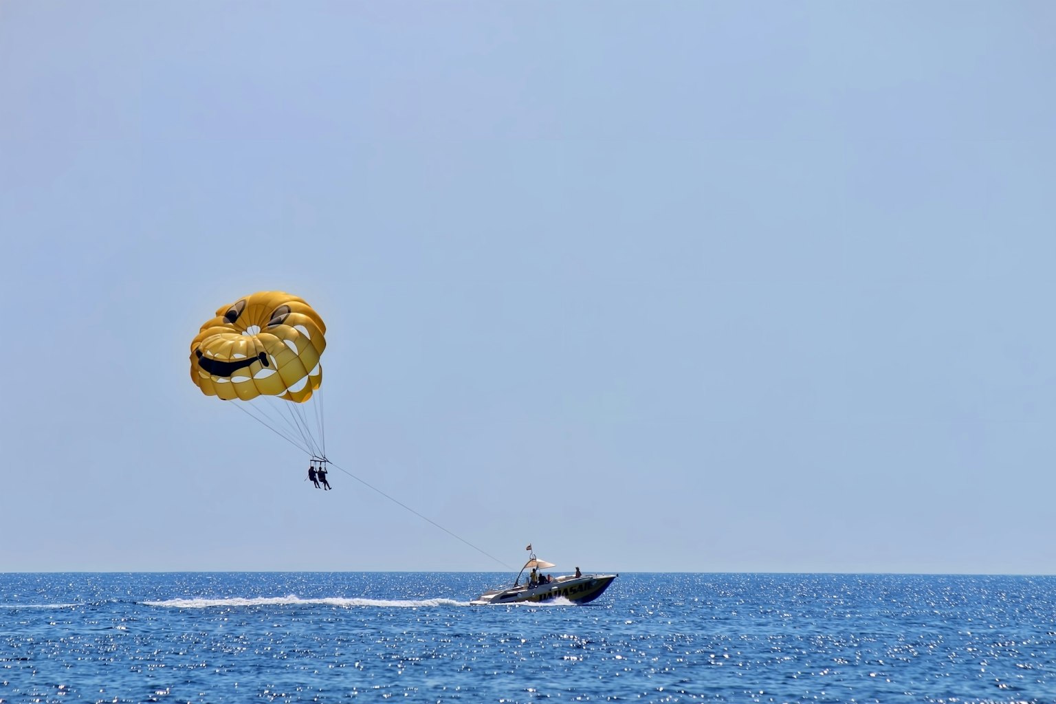 Dua orang parasailing dengan parasut kuning di atas lautan dan perahu di bawahnya