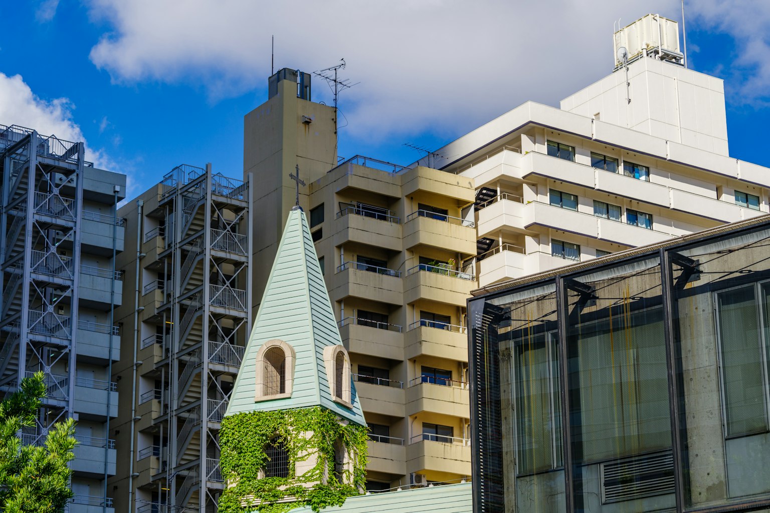 Paesaggio urbano con edifici moderni e una torre di chiesa con vegetazione