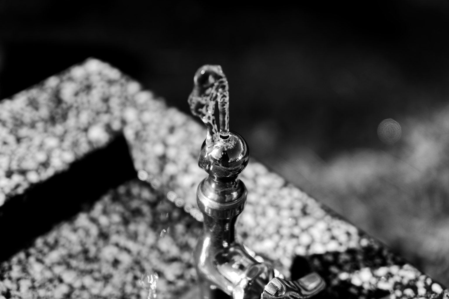 Black and white image of a faucet on a stone pedestal