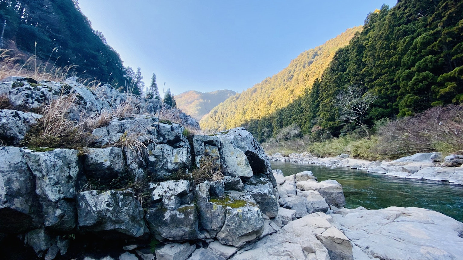 藍天之下被山脈環繞的風景如畫的河流景觀，散落的岩石和郁郁蔥蔥的綠地