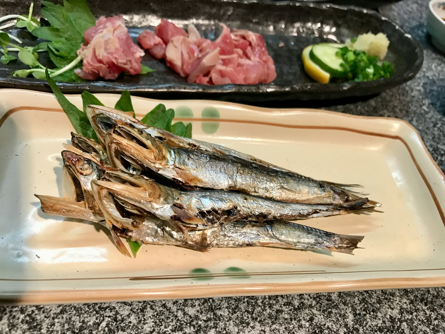 Cá nướng trên đĩa với thịt sống và lát chanh ở phía sau