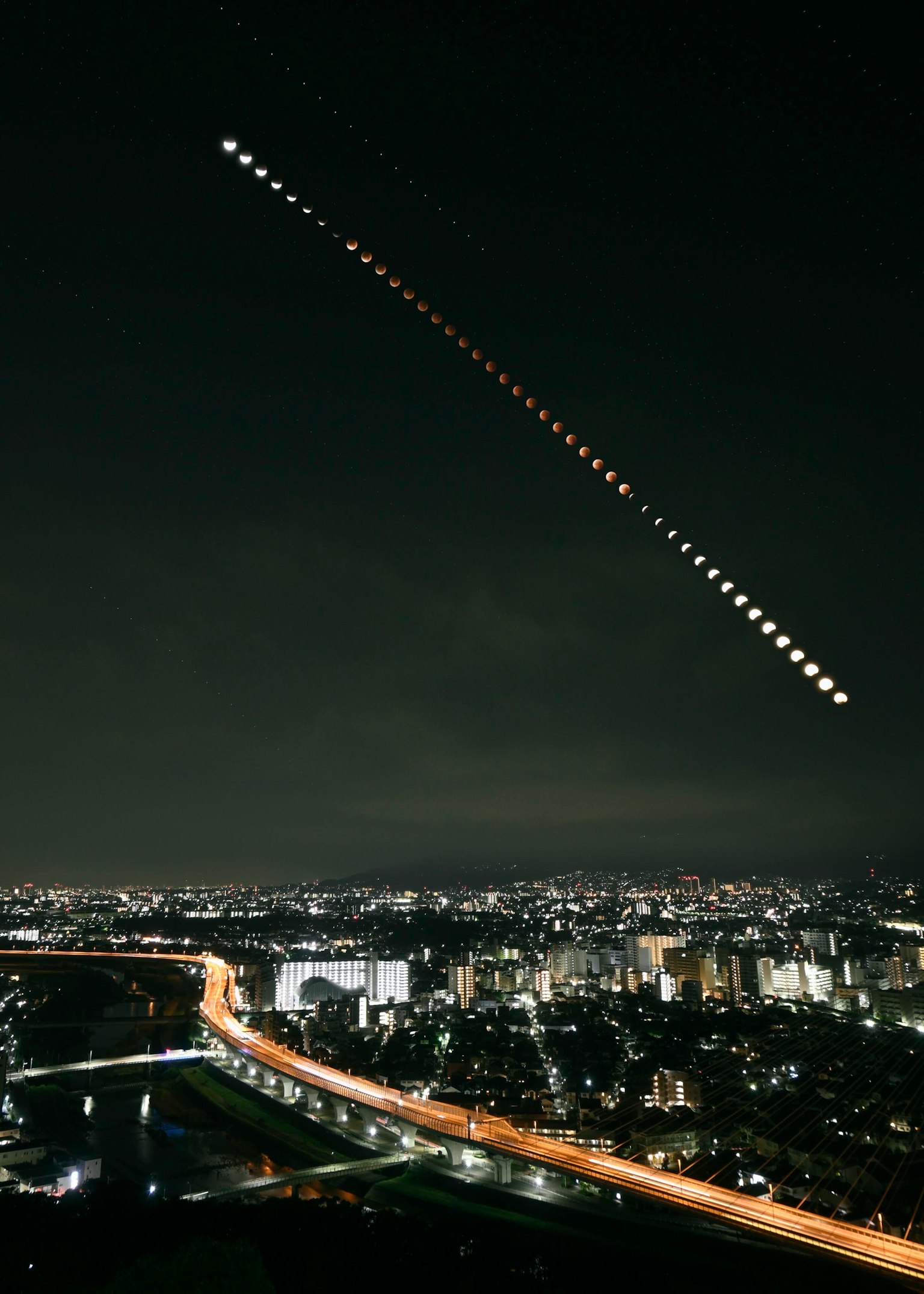 夜空に月の軌跡が描かれた都市の風景