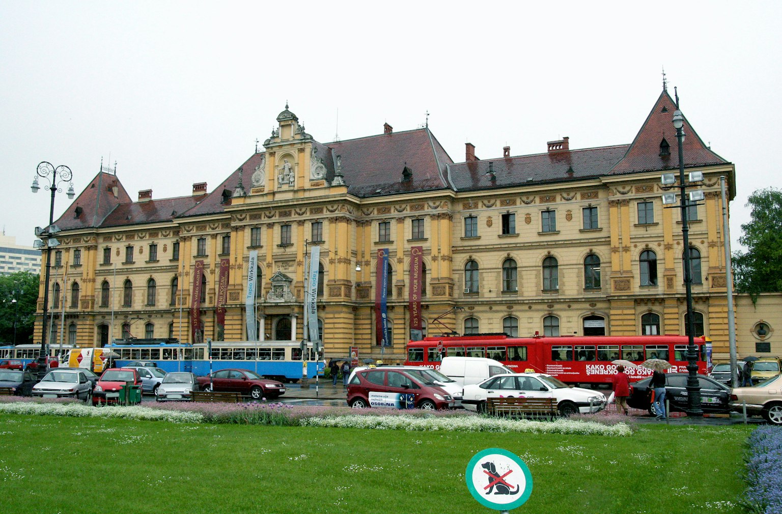 Historisches Gebäude mit gelber Fassade und rotem Dach mit Autos und Straßenbahnen