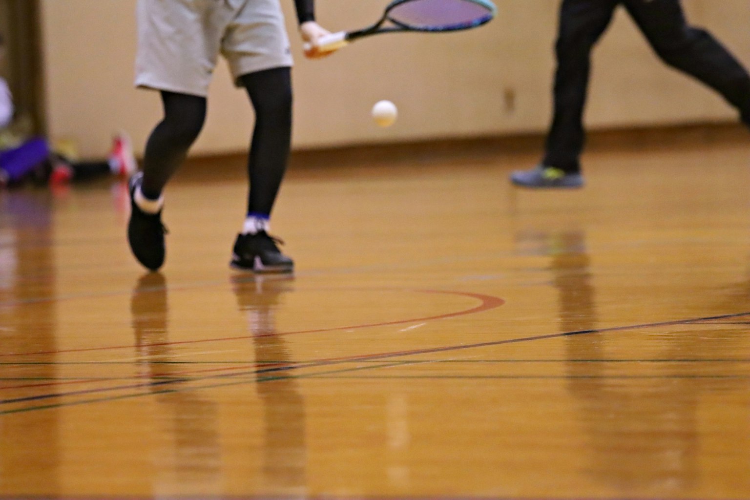 Un giocatore colpisce una palla con una racchetta da tennis su un pavimento di legno in palestra