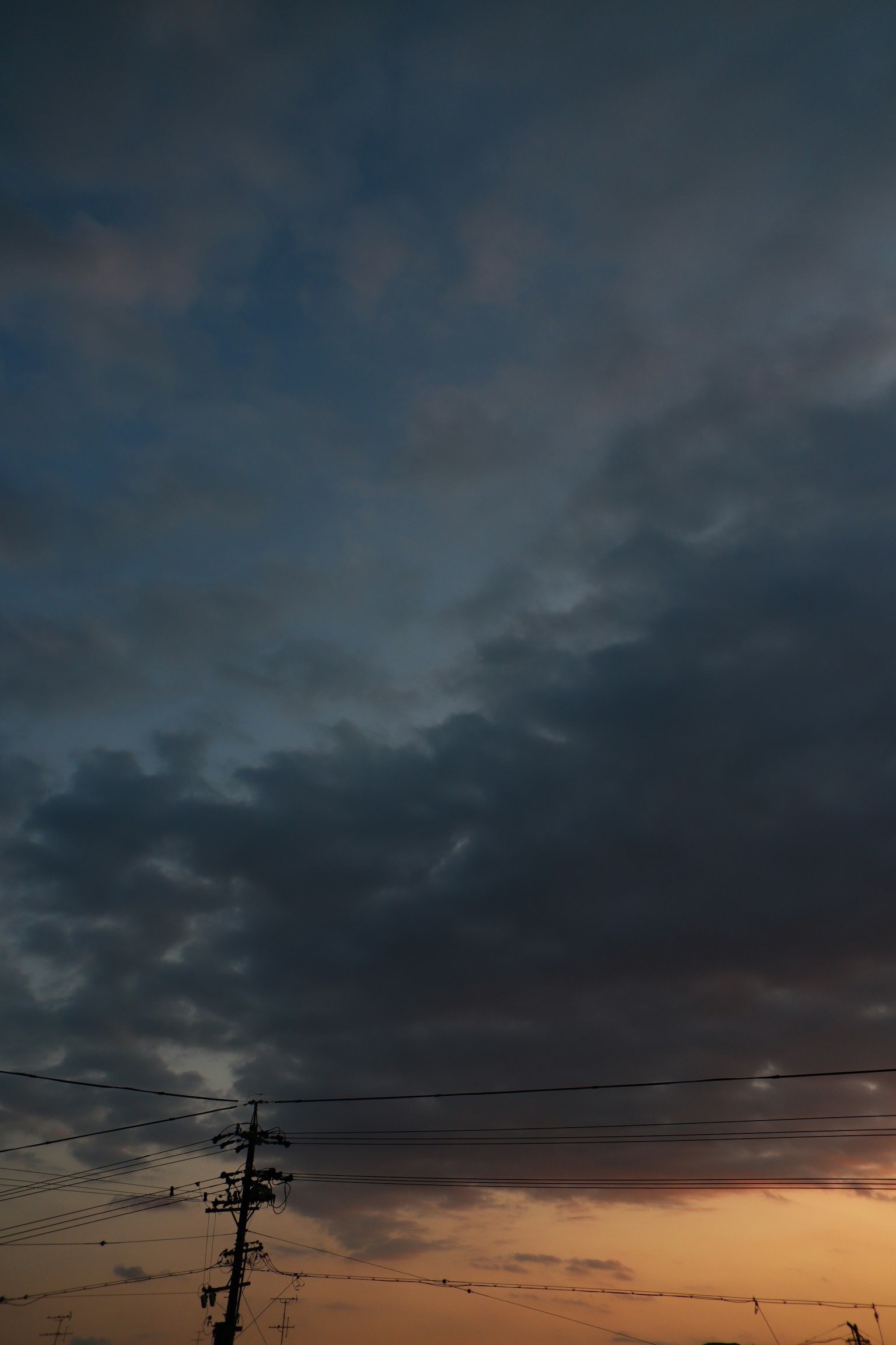 Cielo al tramonto con nuvole scure e un palo della luce