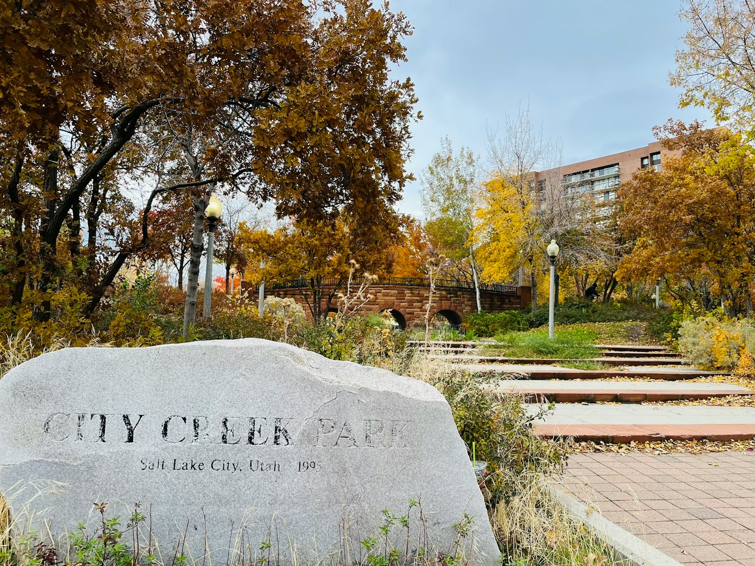 Monumento de piedra con la inscripción CENTRO DE LA CIUDAD rodeado de follaje de otoño y senderos