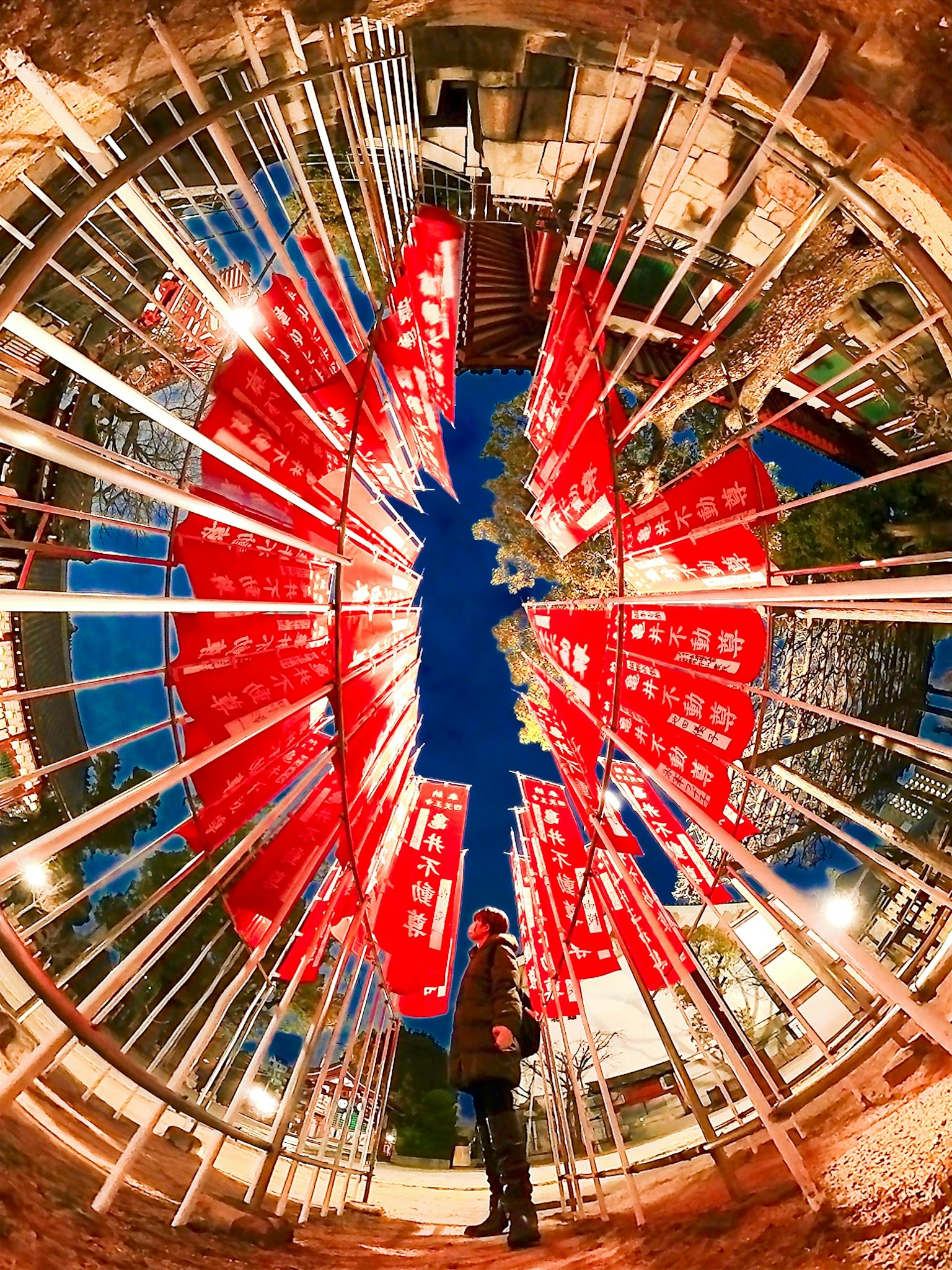 Image of a person standing in a shrine courtyard surrounded by red flags