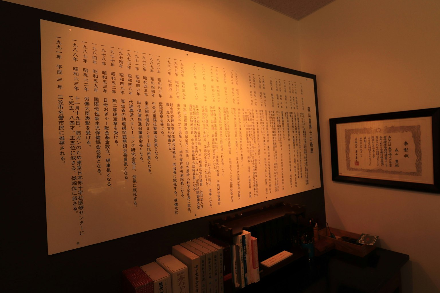 Une photo d'un mur affichant du texte avec des livres sur une étagère et un document encadré