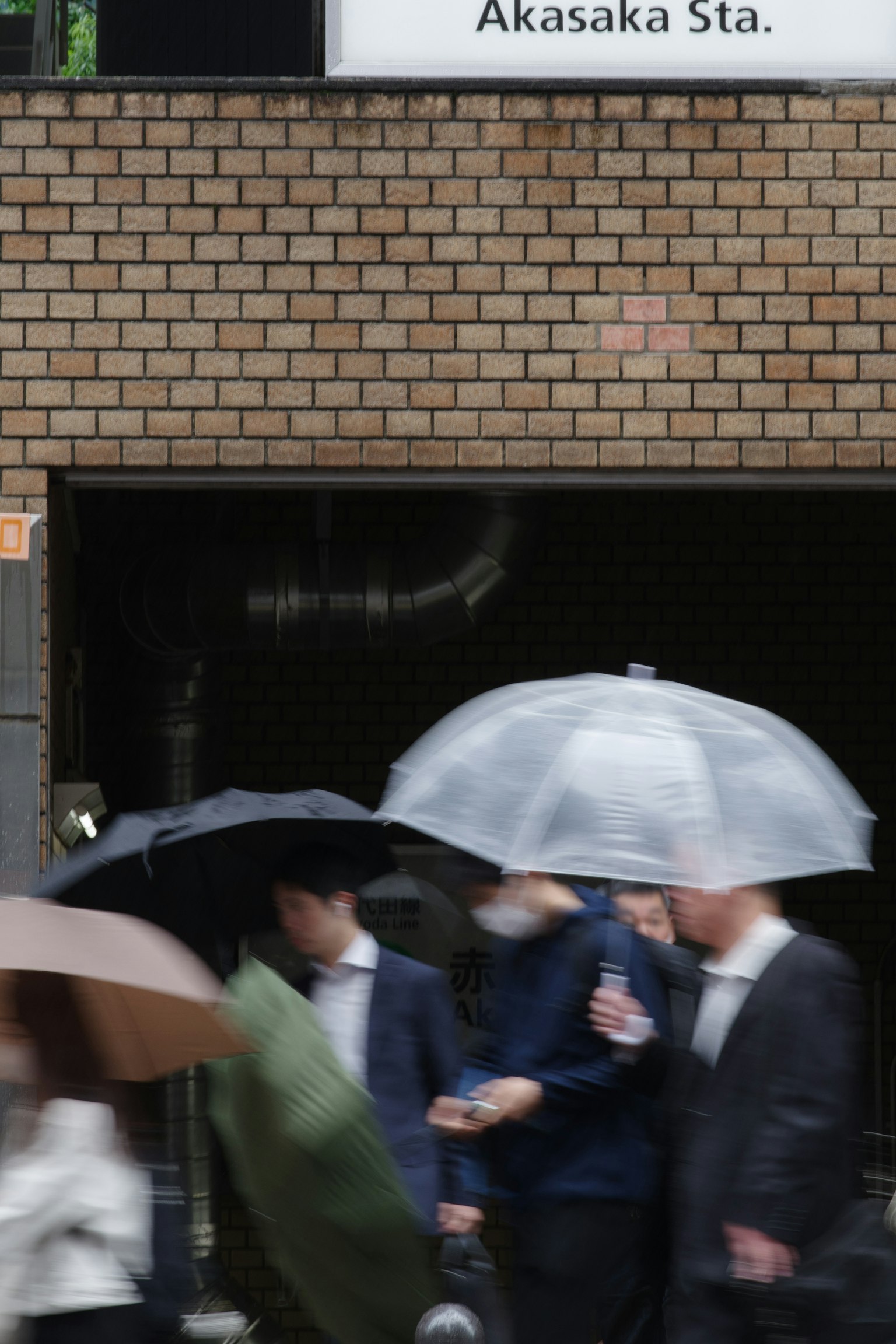 Persone con ombrelli si riuniscono alla stazione Akasaka sotto la pioggia
